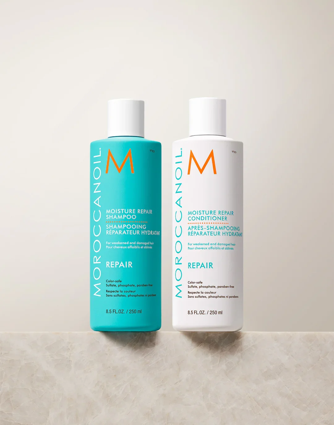 Two bottles of Moroccanoil moisture repair hair products, one shampoo in blue packaging and one conditioner in white packaging, against a dark background.