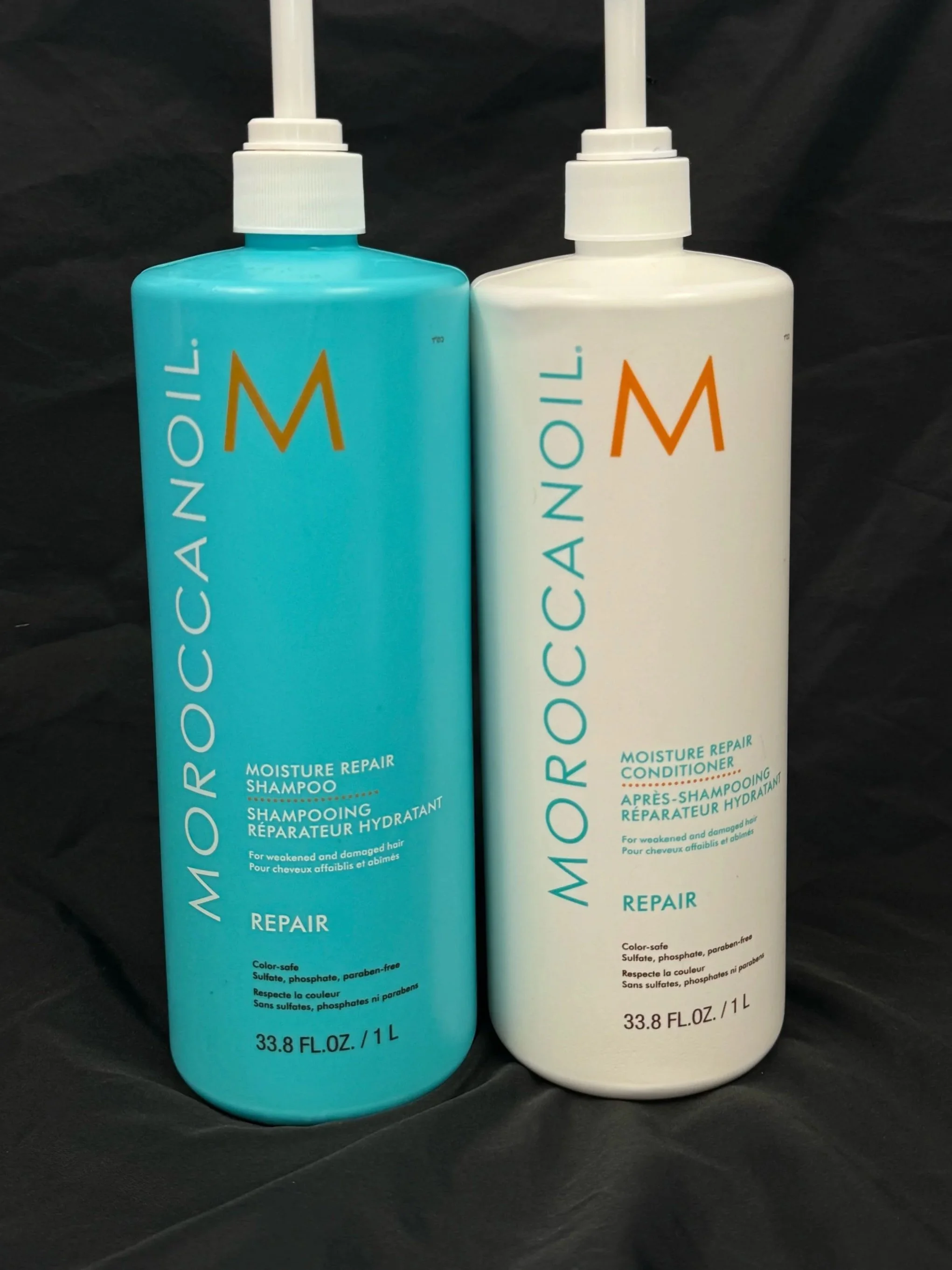 Two bottles of Moroccanoil moisture repair hair products, one shampoo in blue packaging and one conditioner in white packaging, against a dark background.