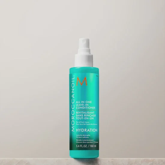 A blue bottle of Moroccanoil All-in-One Leave-in Conditioner with white pump dispenser, placed on black fabric background.