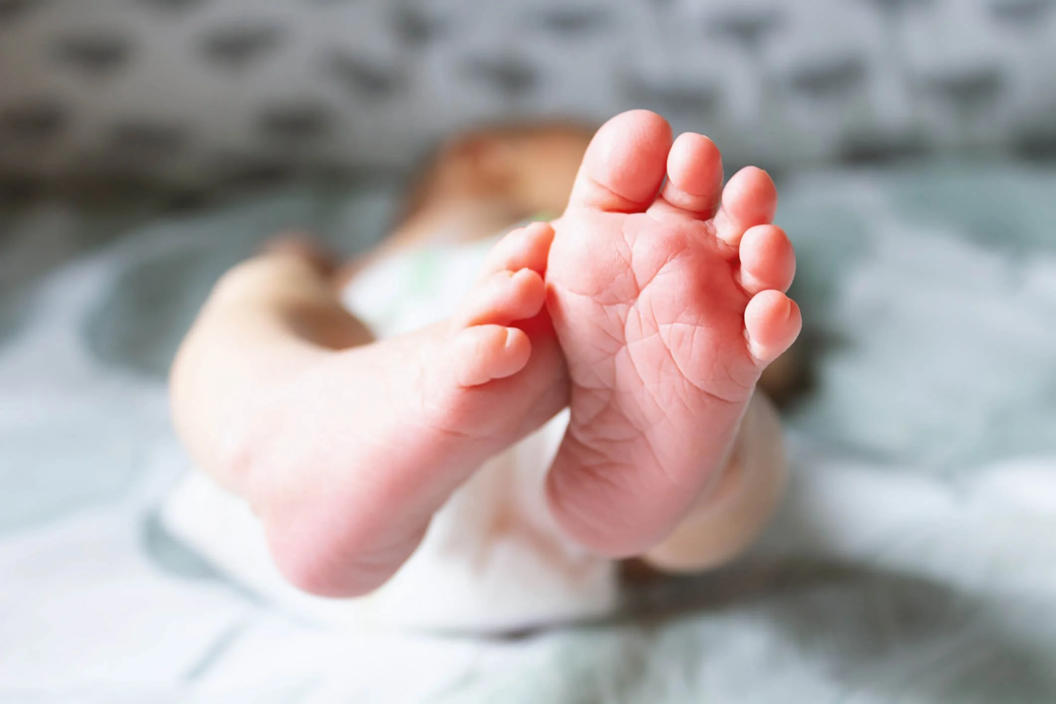 Close-up of a baby's foot with toes stretched out, in focus, with a blurred background showing the baby's face and water.
