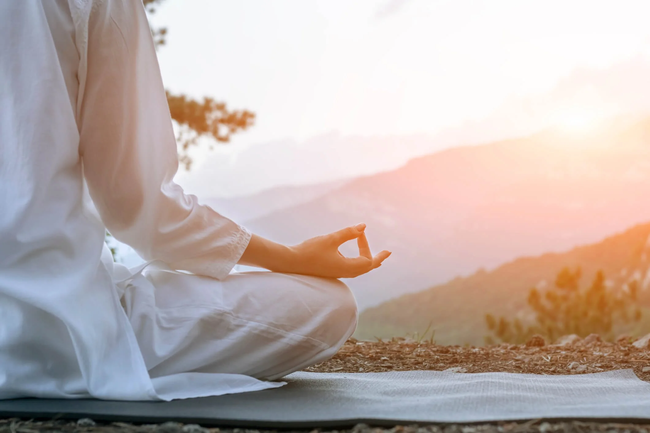 Person practicing meditation outdoors during sunset, sitting cross-legged on a mat with hand in mudra position.