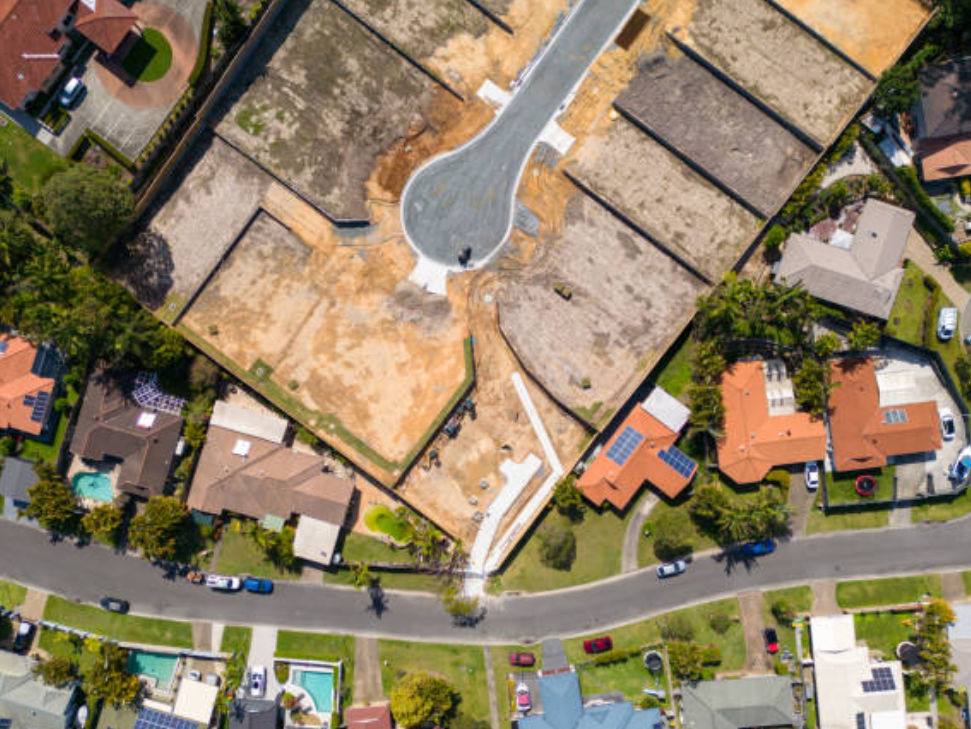 Vista aérea de una construcción residencial en proceso, con varias casas alrededor y una calle en primer plano.