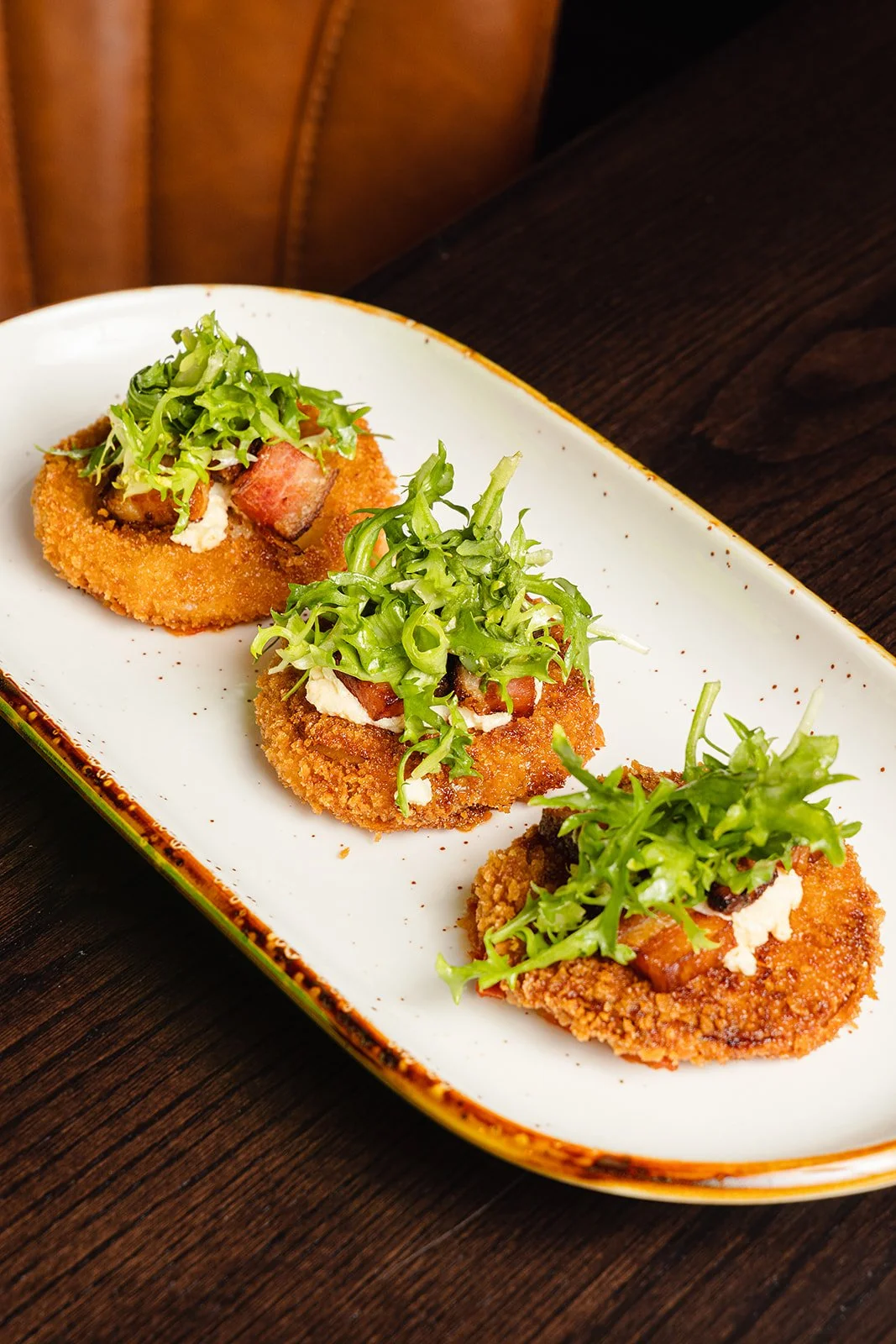 Three breaded fried appetizers topped with chopped green lettuce and a dollop of white sauce on a white oval plate.