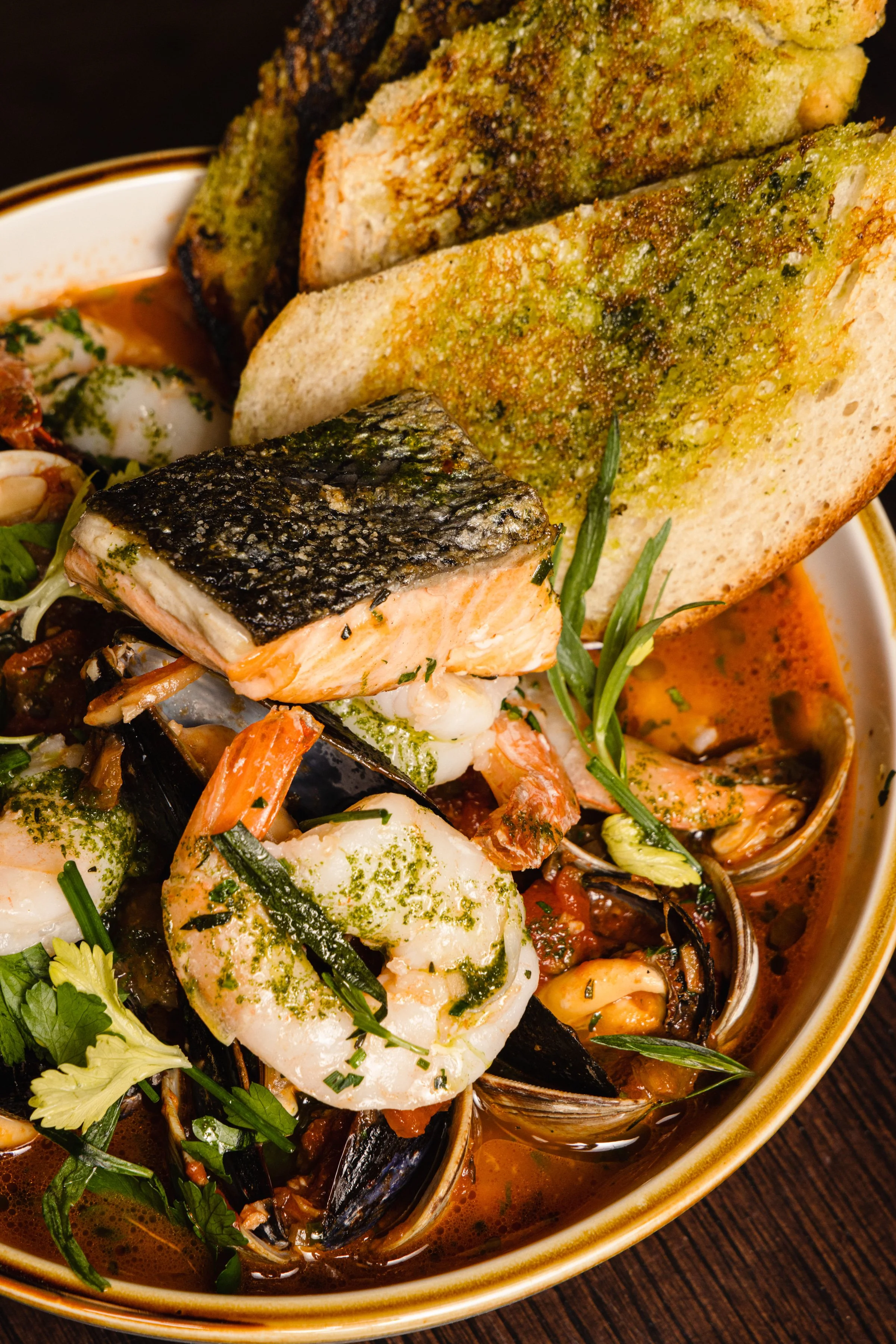 Seafood stew with shrimp, salmon, and mussels, garnished with herbs, accompanied by slices of garlic bread.