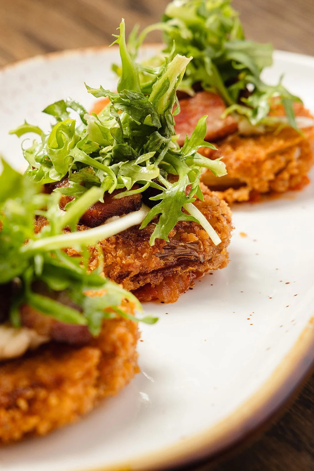 Close-up of fried chicken topped with fresh greens on a white oval plate.