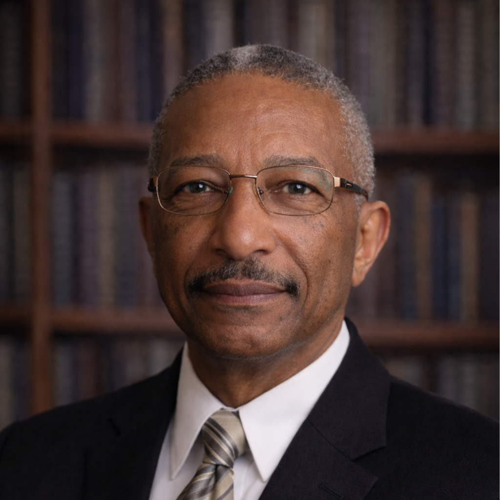 Portrait of an older man with glasses, wearing a suit and tie, standing in front of a bookshelf filled with books.