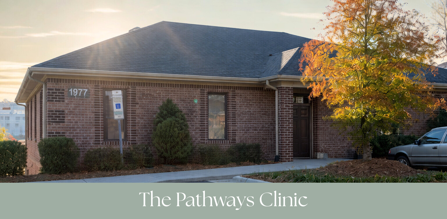A brick building with the numbers 1977 on the wall, trees with fall foliage, parked car, and a sidewalk. The text overlay reads "The Pathways Clinic."