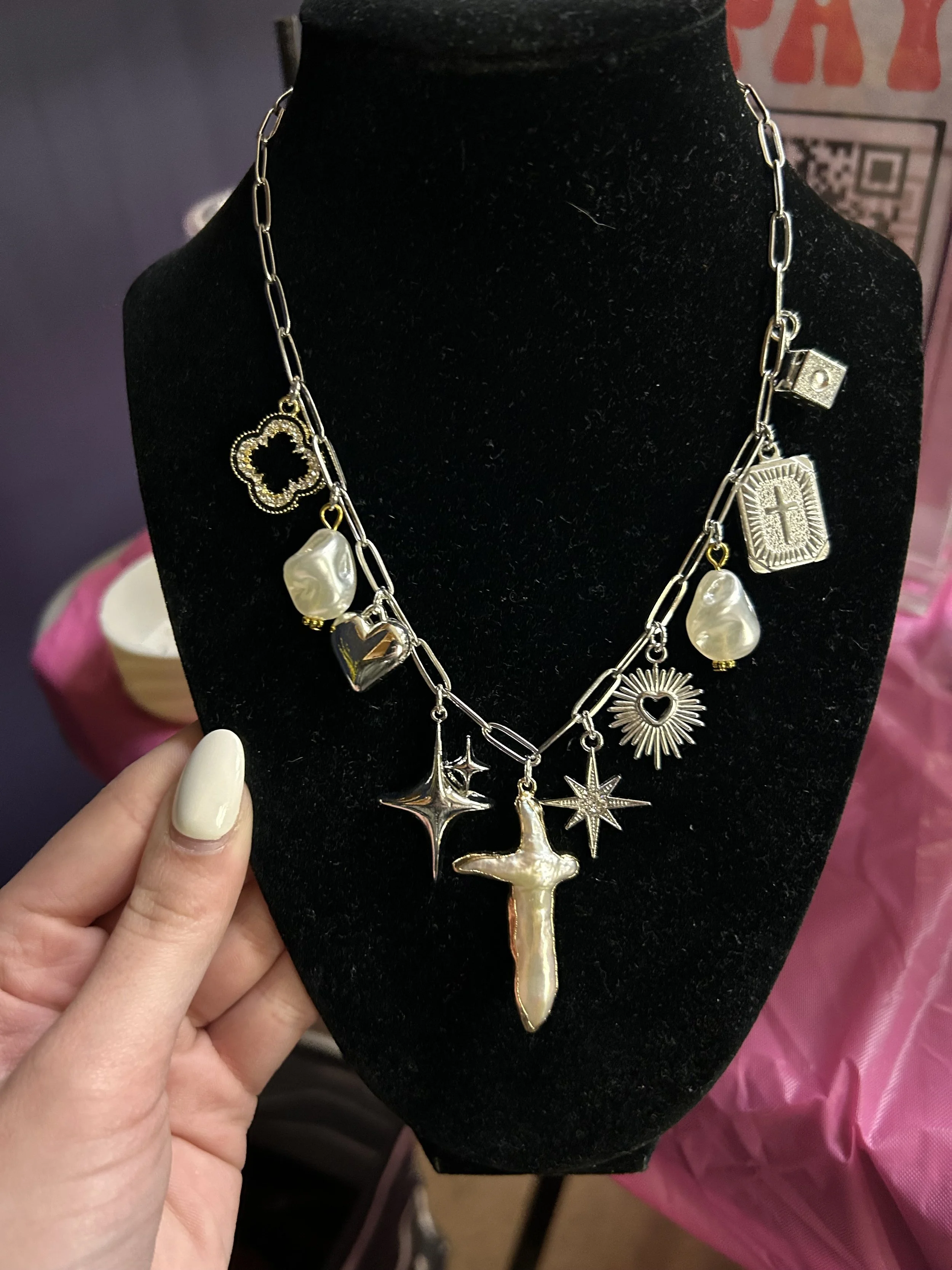 Silver necklace with various religious, star, and pearl charms displayed on a black bust.