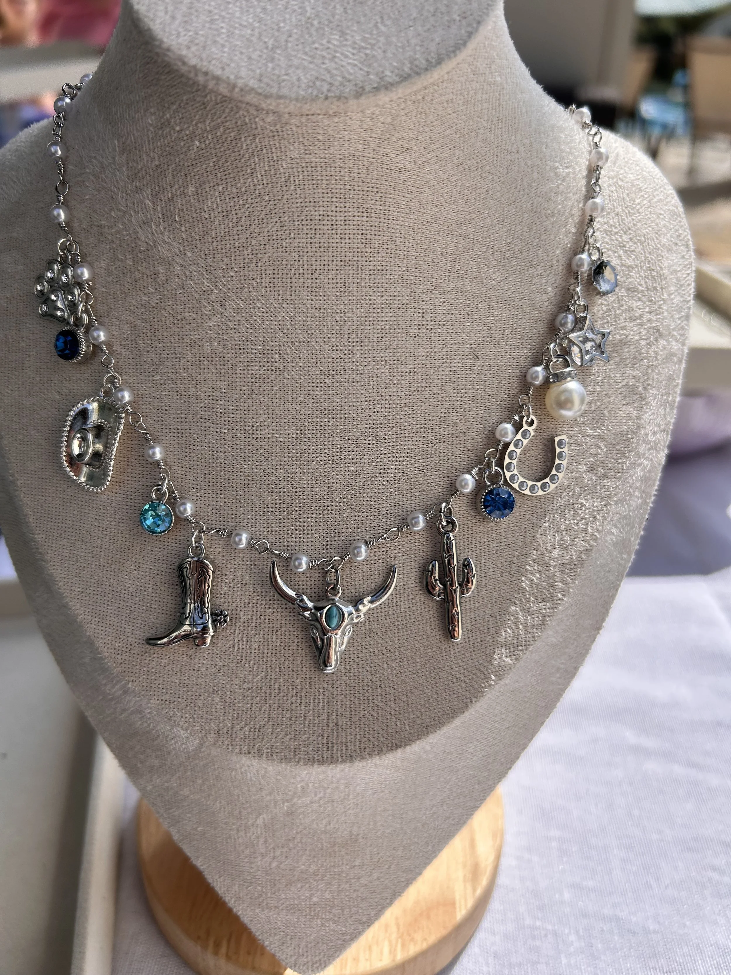 Jewelry necklace with charms including a cowboy hat, bison head, horseshoe, boot, cactus, and star, displayed on a beige bust form.
