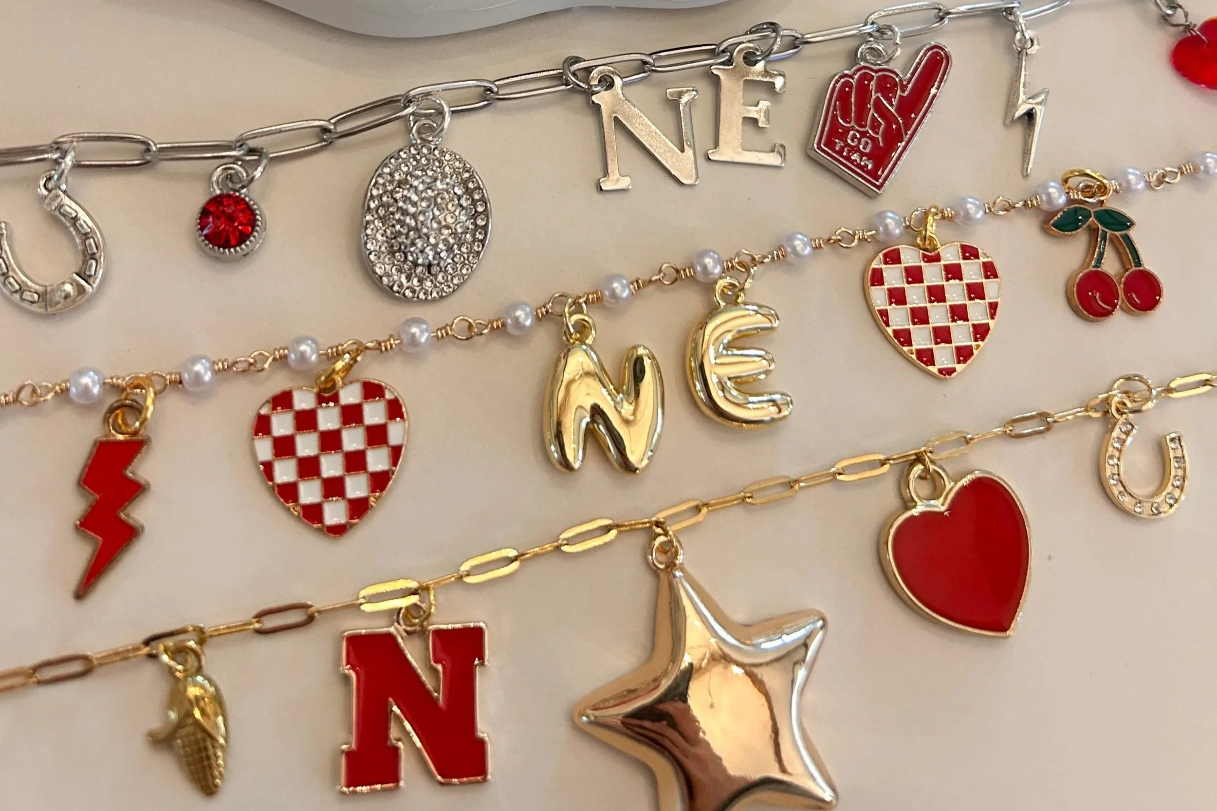 Several layered gold and silver charm bracelets with various charms including hearts, letters, a star, and a lightning bolt.