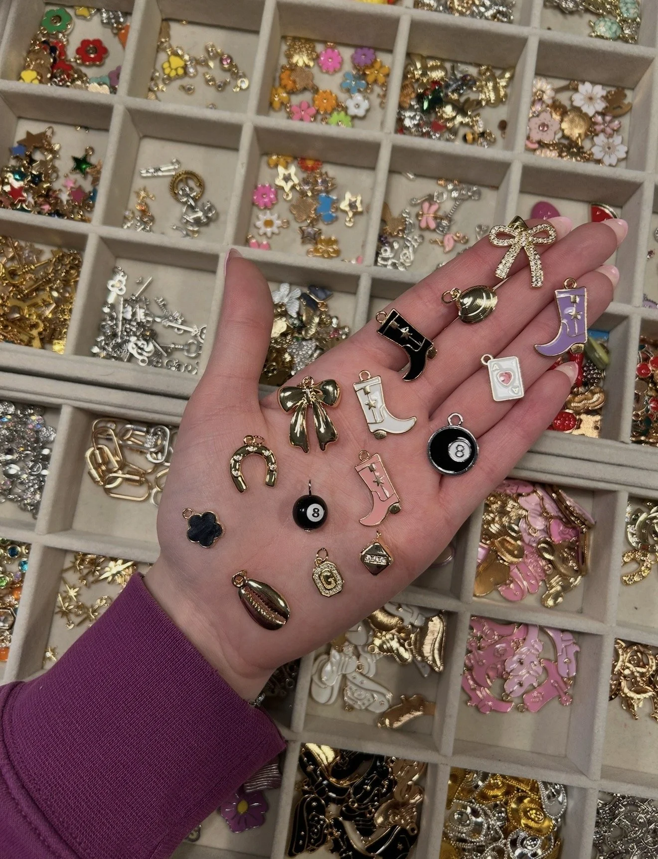 A hand holding various small, colorful charms with a jewelry box filled with more charms in the background.