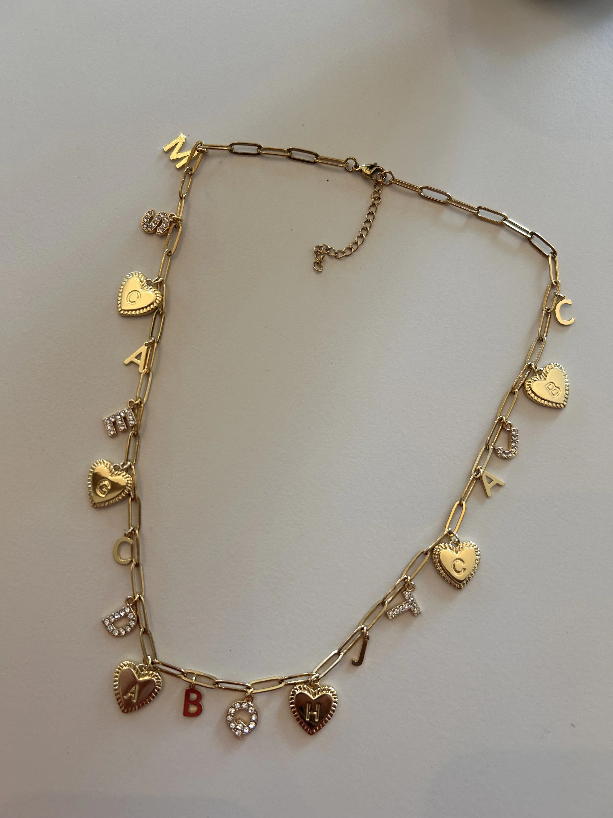 Gold chain necklace with heart-shaped and letter charms, some with rhinestones.
