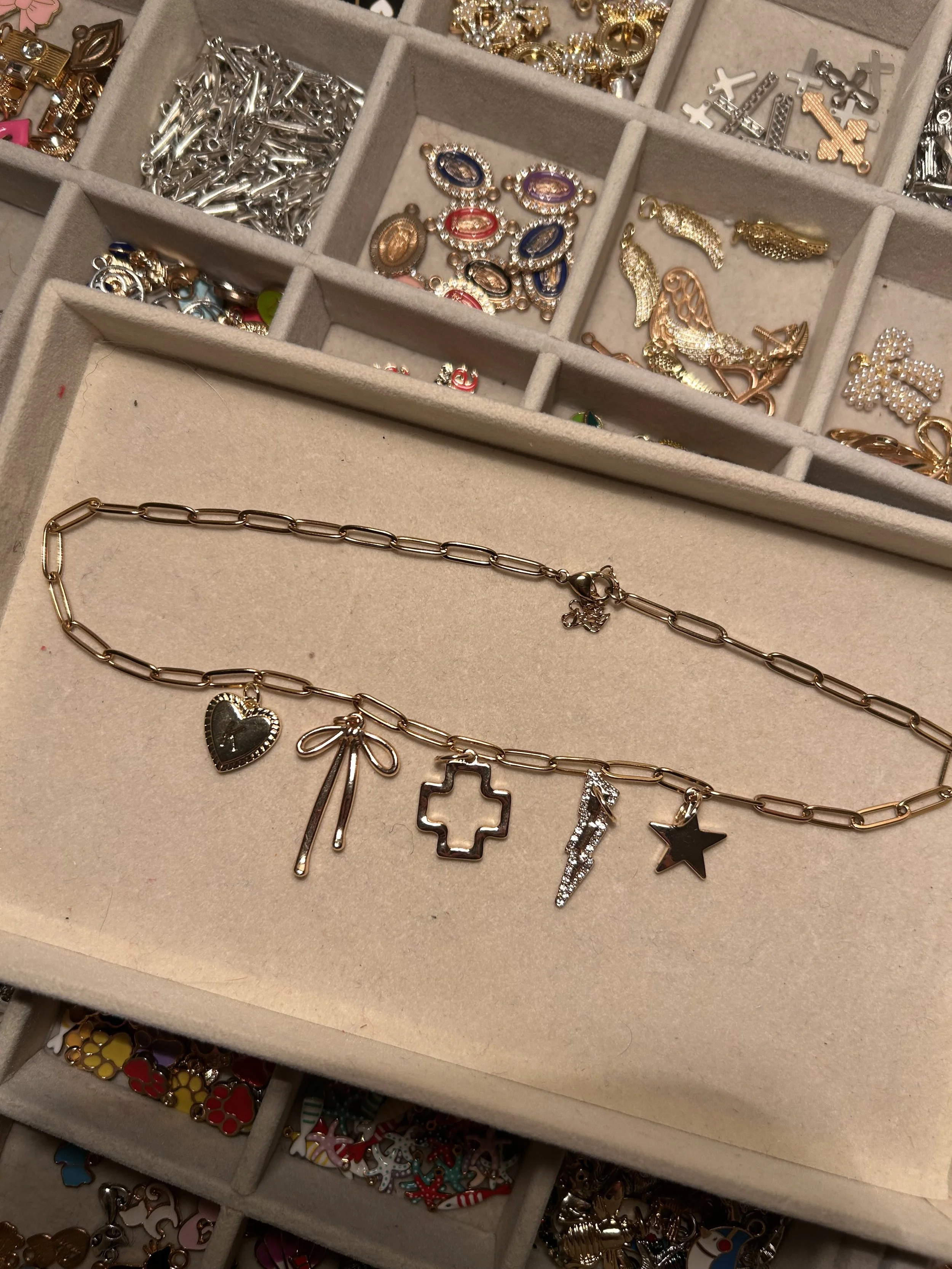 Necklace with assorted charms including a heart, bow, cross, lightning bolt, star, and rhinestone details, displayed on a jewelry organizer.