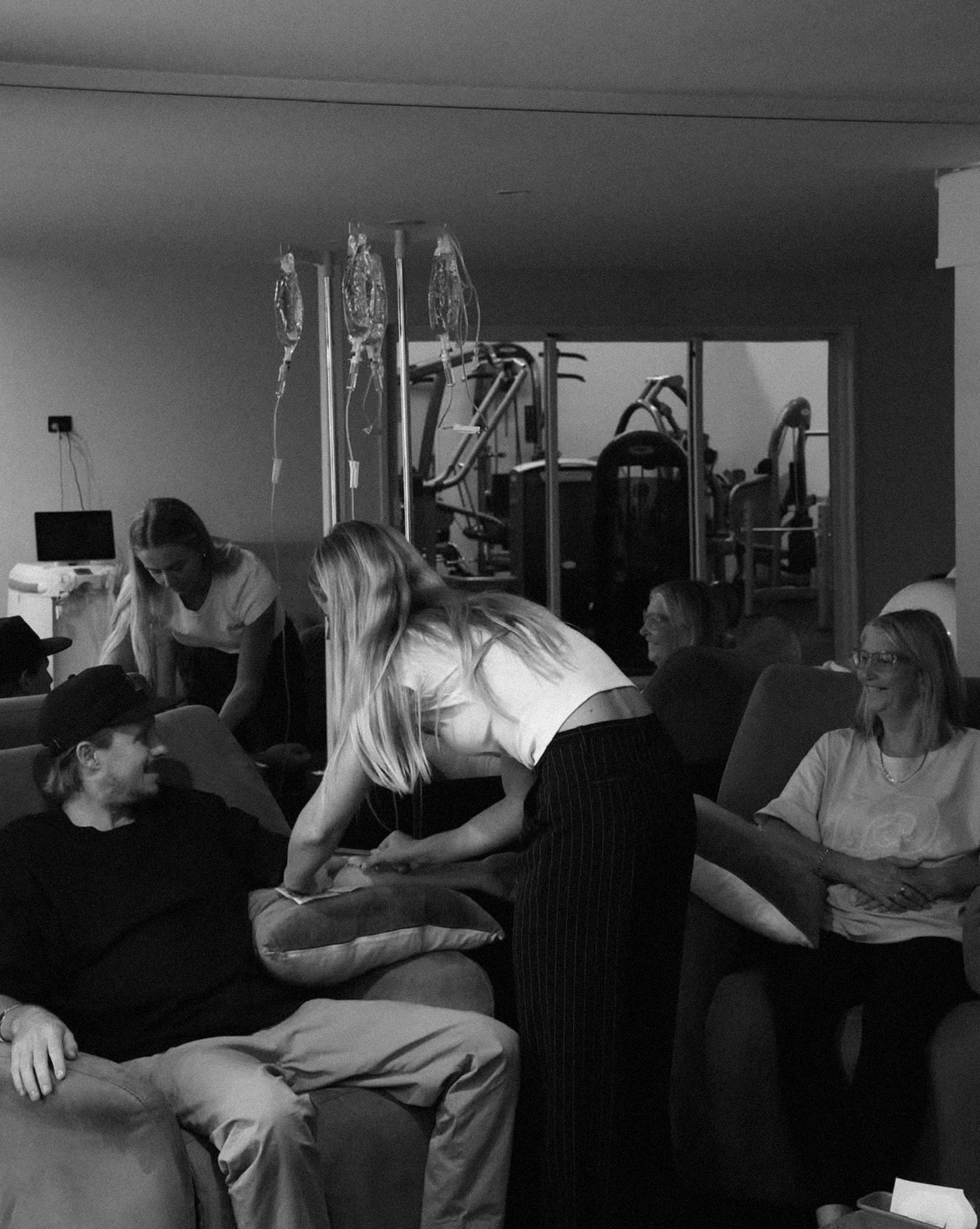 People in a living room participating in a blood donation drive, with IV bags hanging and medical staff assisting.