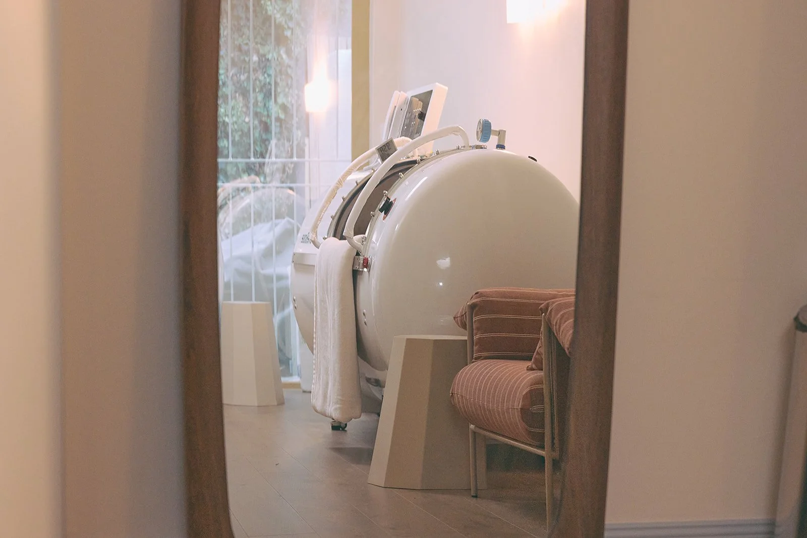 A patient lying on their back inside a medical hyperbaric chamber with a breathing mask, connected to medical equipment and a monitor.