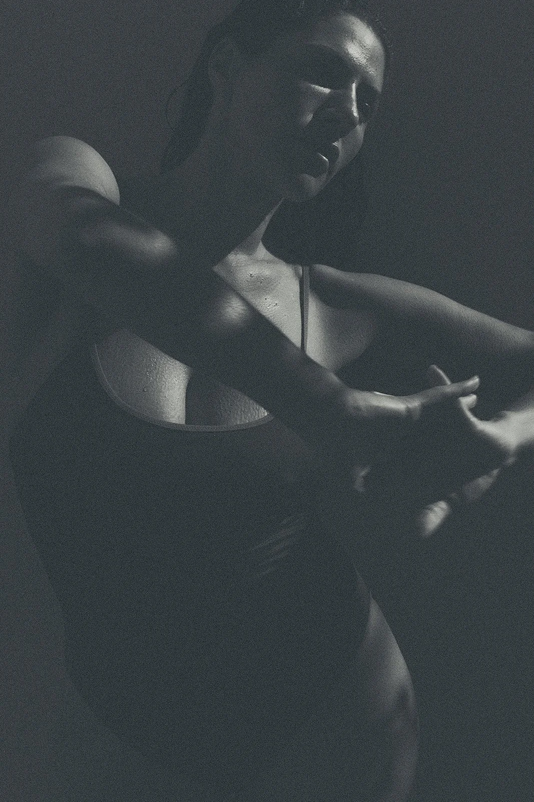 Close-up of a woman's bare shoulder and upper arm, with part of her face and long dark hair visible, in black and white.