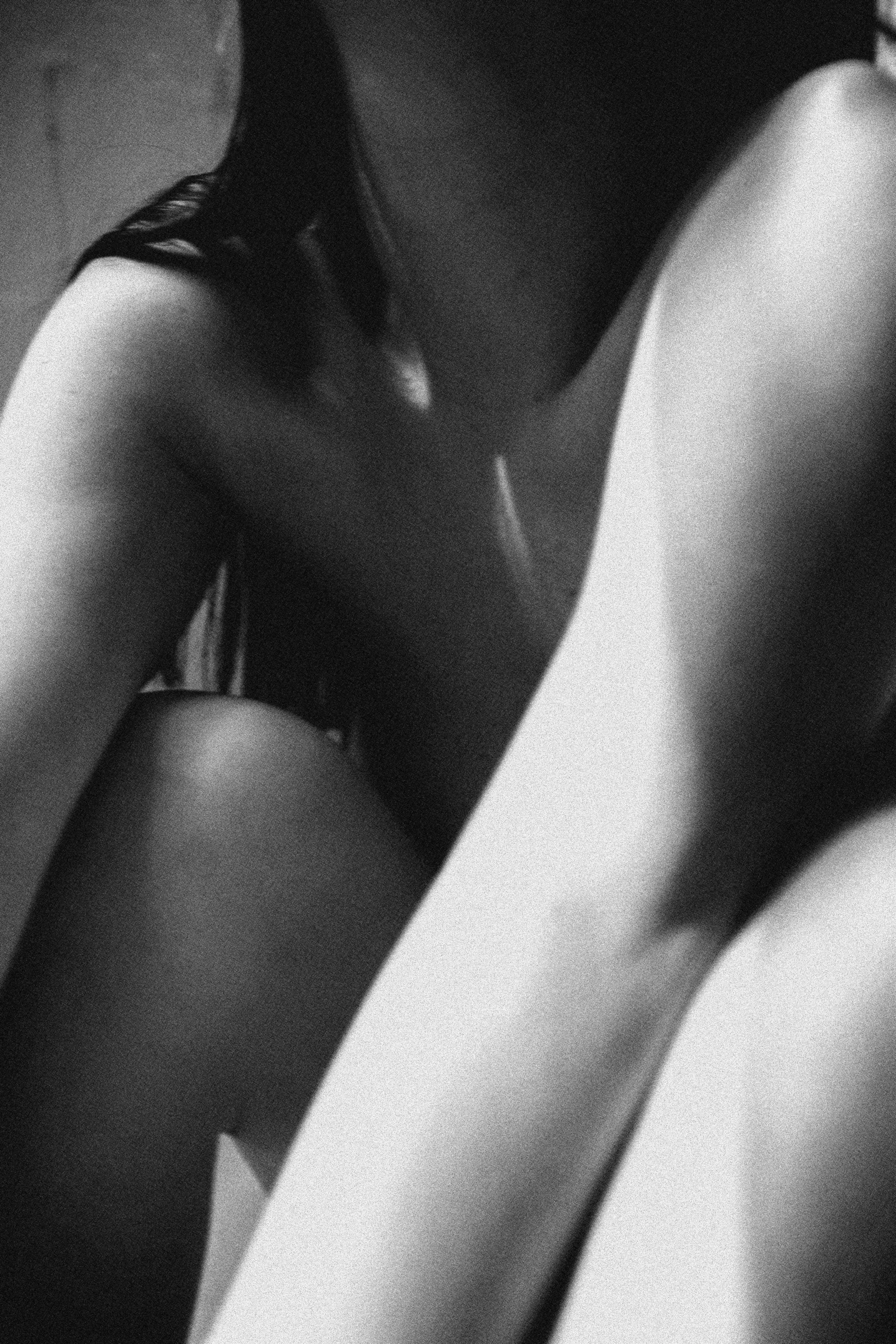 Close-up of a woman's bare shoulder and upper arm, with part of her face and long dark hair visible, in black and white.