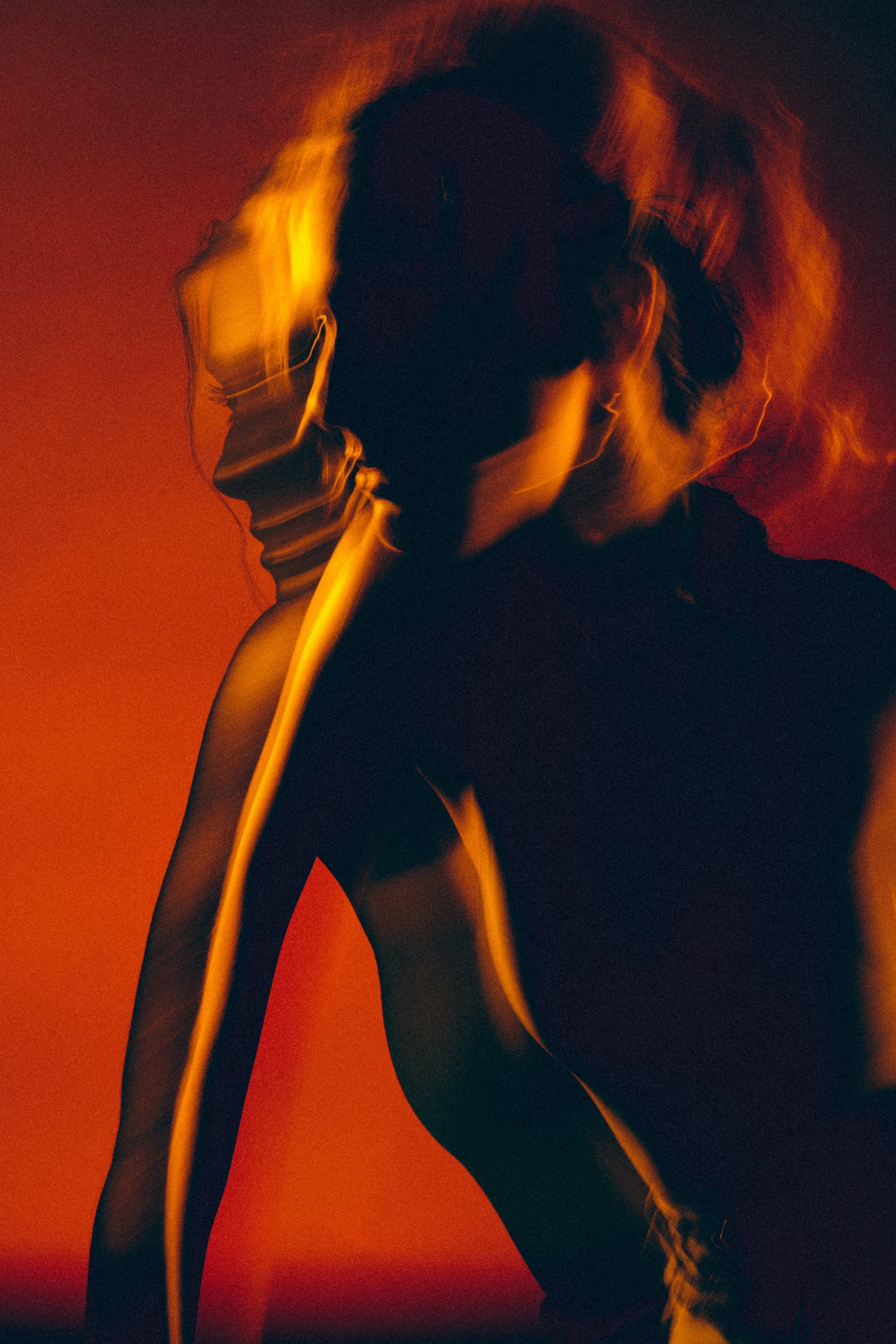 A silhouette of a woman with blurred motion and orange lighting in a dark background.