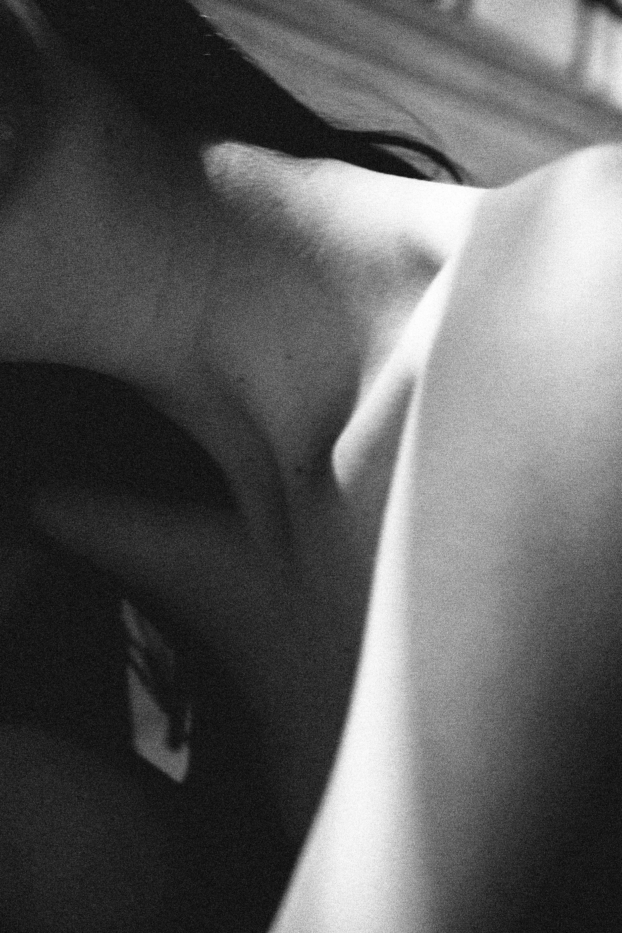 Close-up black and white photograph of a person's face with eyes closed, partially obscured by sharp shadows and lighting.