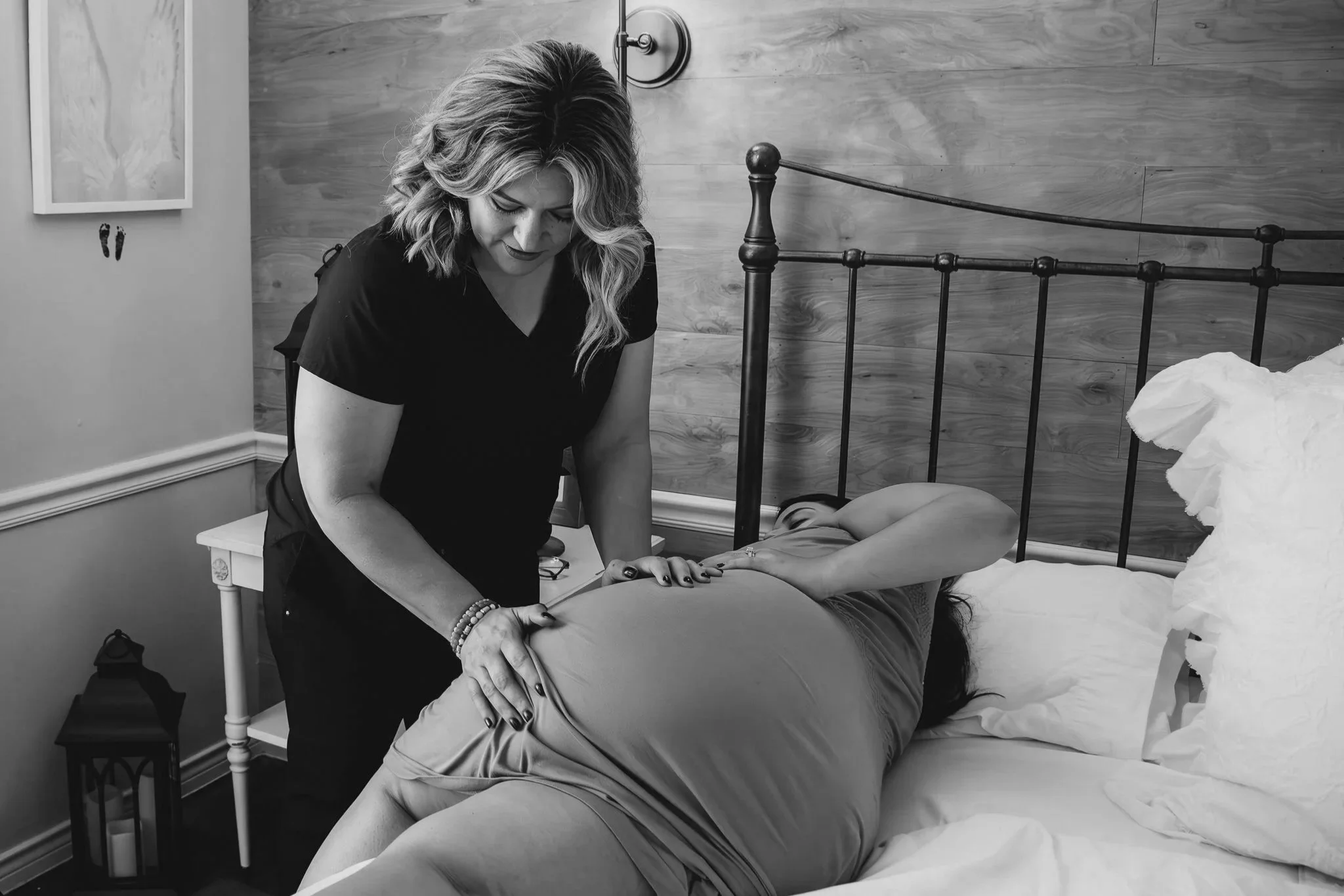 A woman receiving a medical checkup or massage from a healthcare provider or therapist in a bedroom setting.
