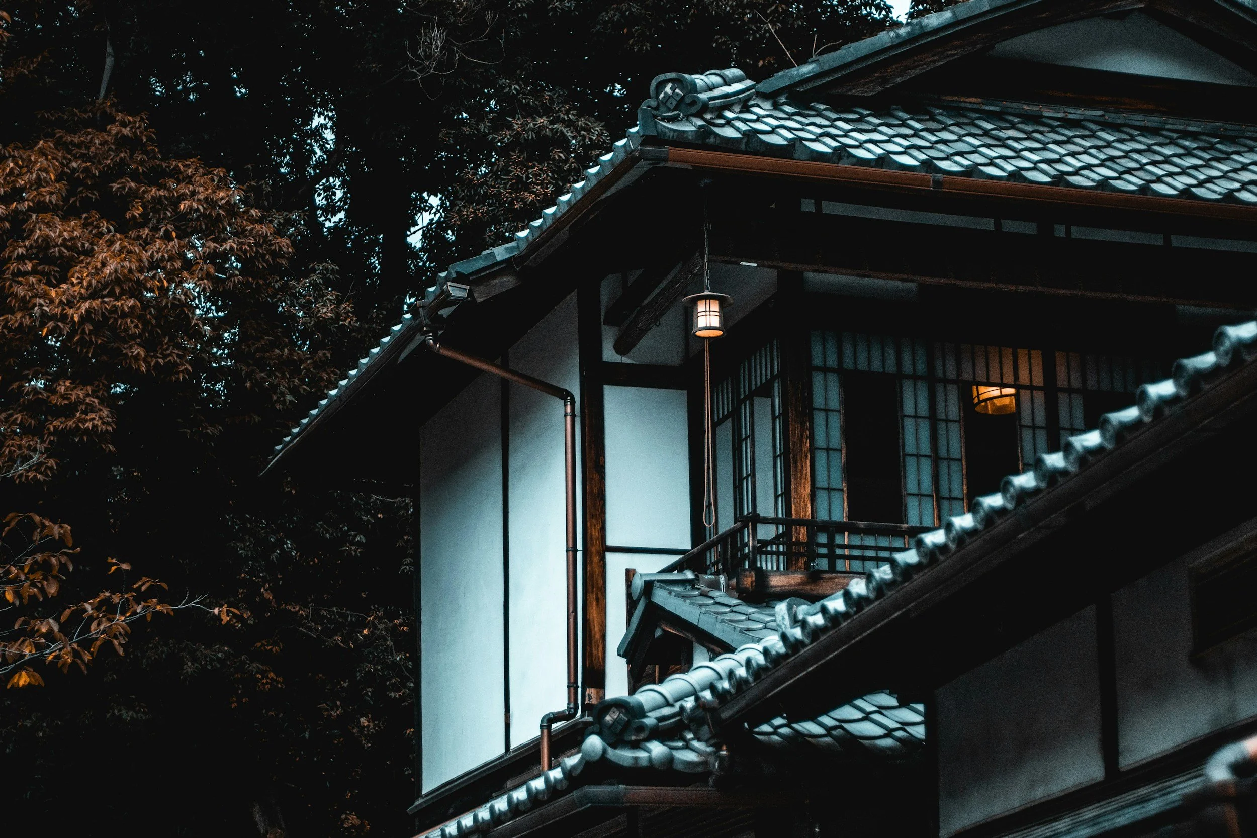 夕暮れに灯りがともる、日本の古い実家・空き家の軒先。海外在住者のお客様も守りたい故郷の記憶と不動産資産のイメージ