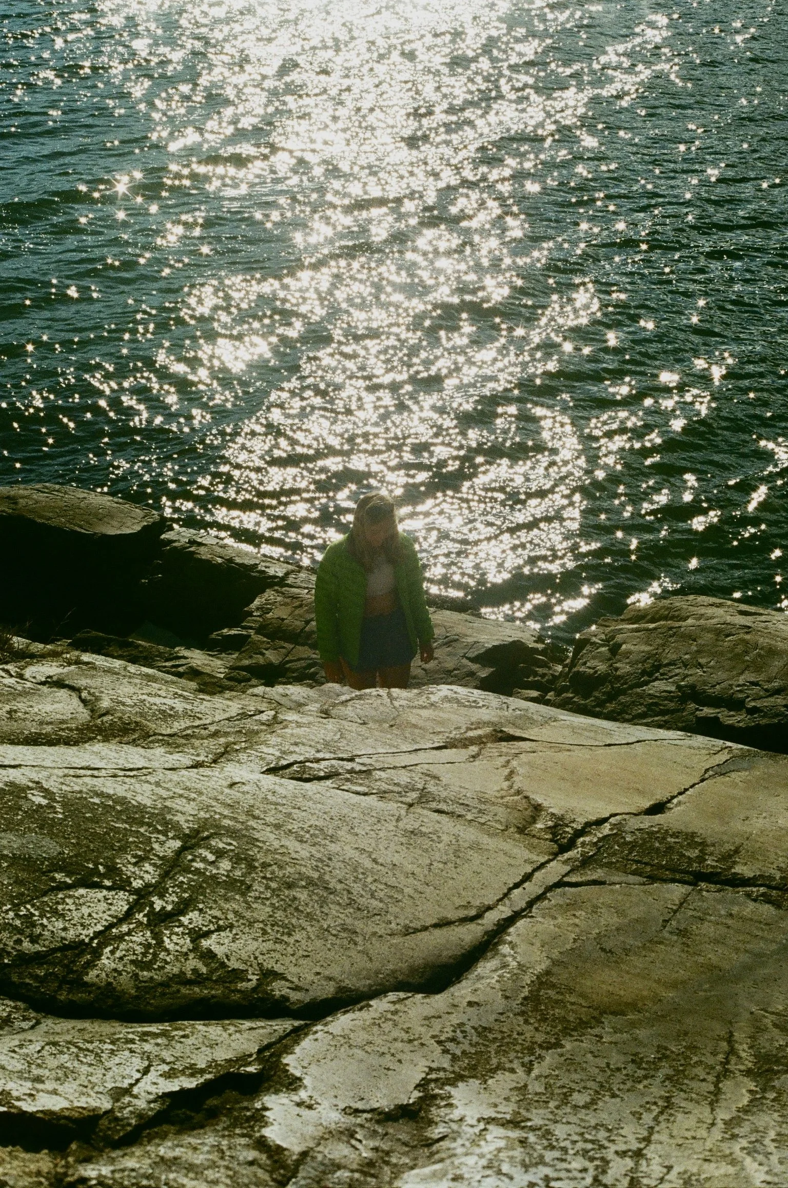 A person standing on rocks near the water, with sunlight reflecting off the surface.
