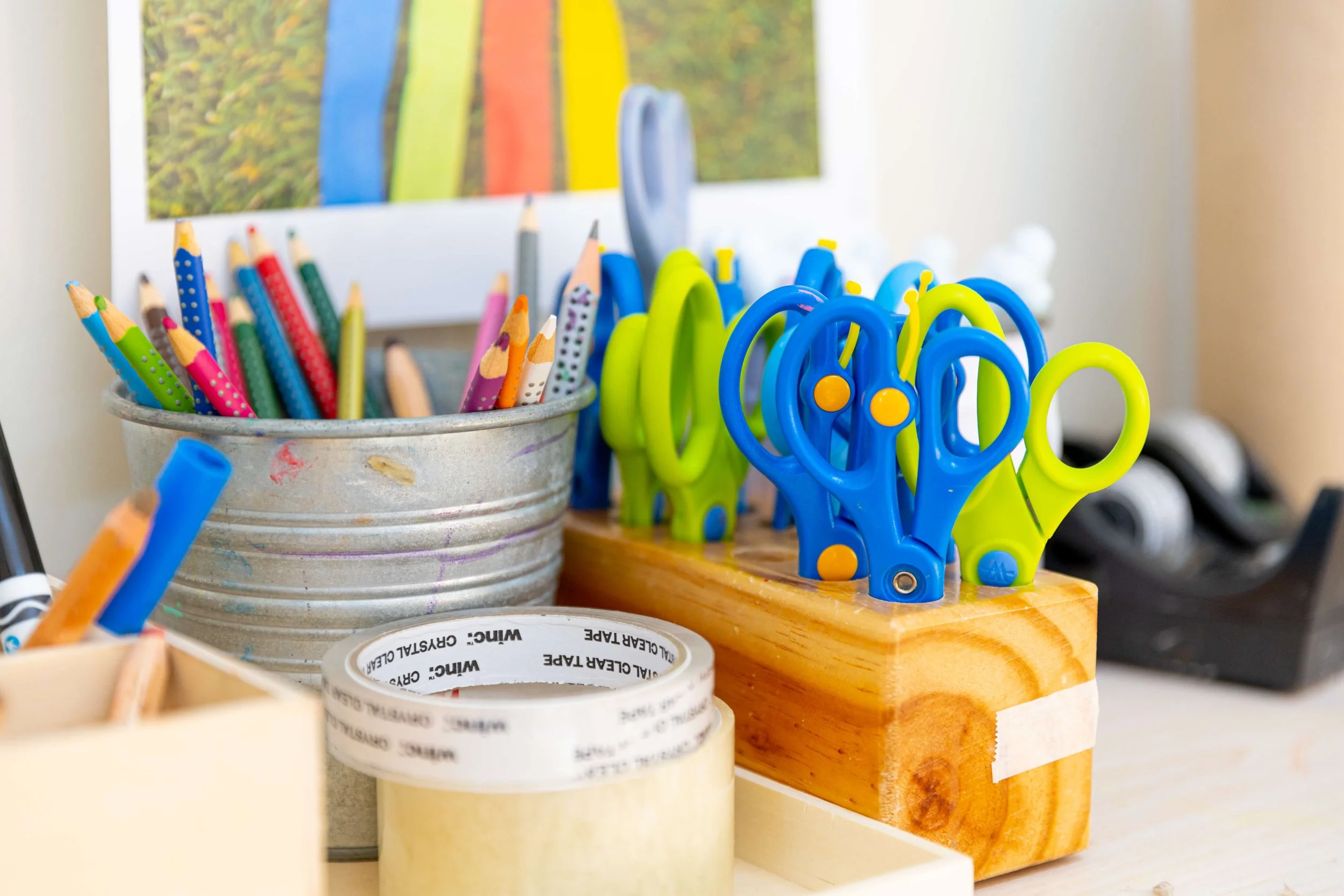 Colorful children's scissors and pencils organized in containers on a desk.