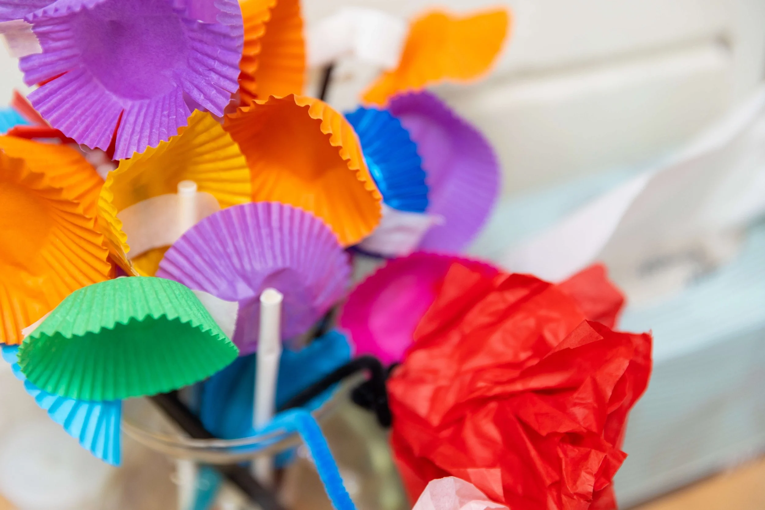 Close-up of colorful paper cupcake liners, including purple, orange, green, yellow, pink, and blue, arranged in a glass container.