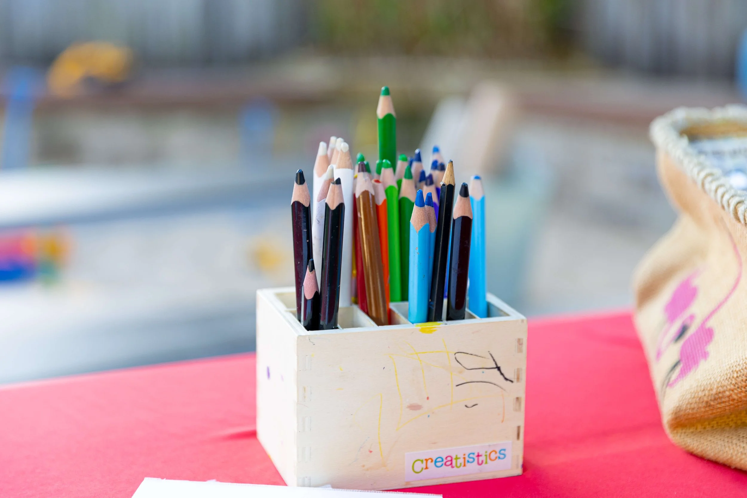 Colorful pencils in a white wooden container on a pink surface