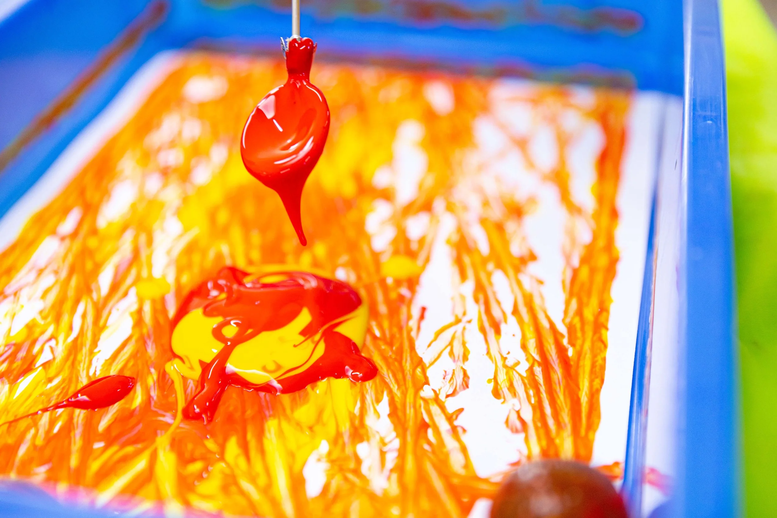 Close-up of bright yellow and red liquid paint dripping inside a blue container.
