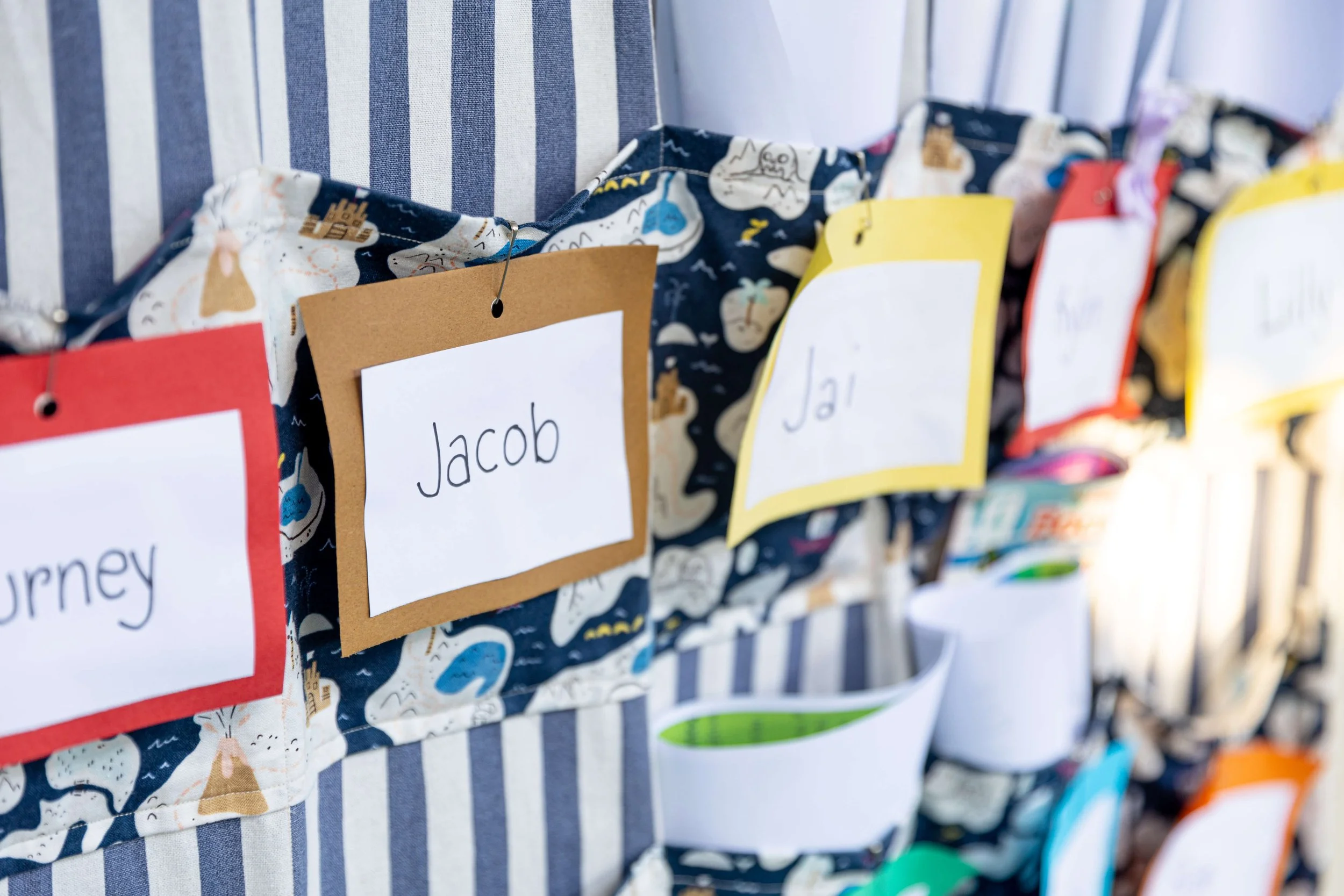 Colorful fabric pockets with name tags, including one labeled 'Jacob', hanging in a row.
