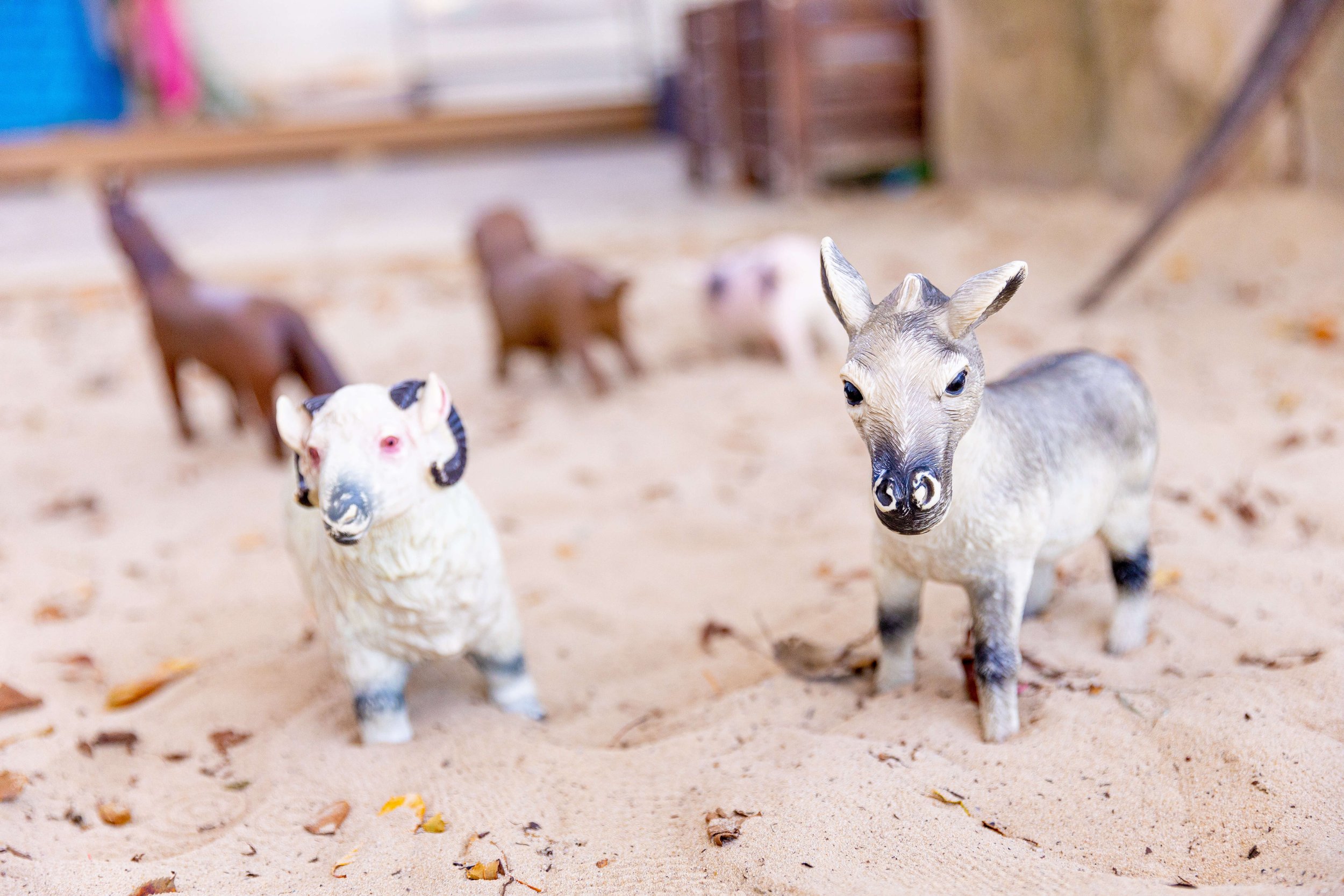 Miniature animal figurines placed on a sandy surface with a blurred background.