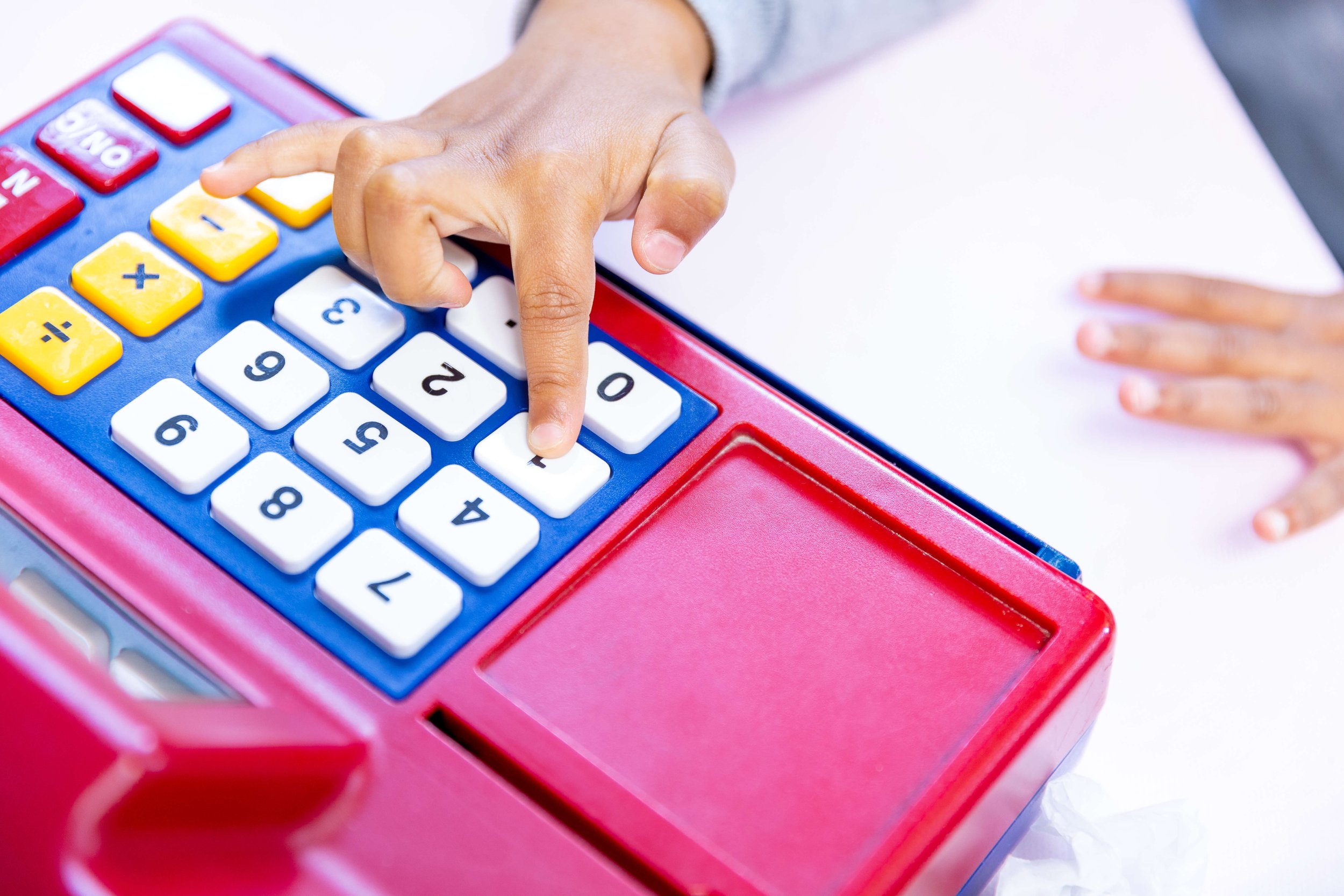 Child pressing buttons on a red and blue cash register with a touch screen interface.