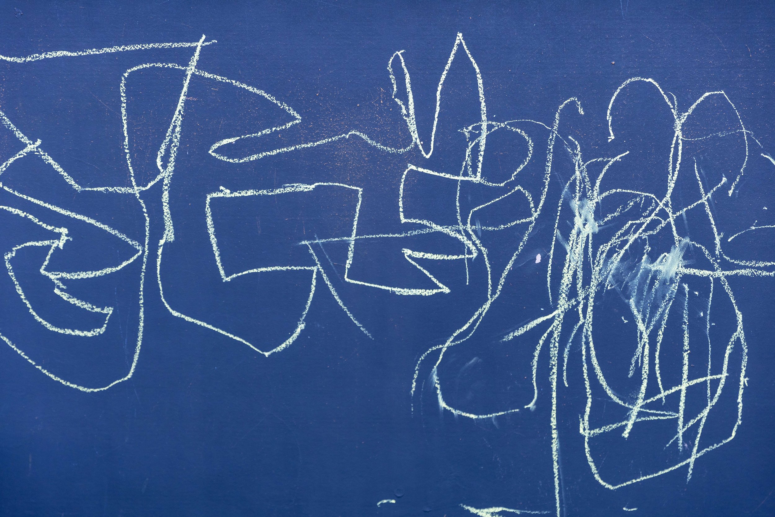 Child's chalk drawing of various abstract shapes and lines on a blue chalkboard.