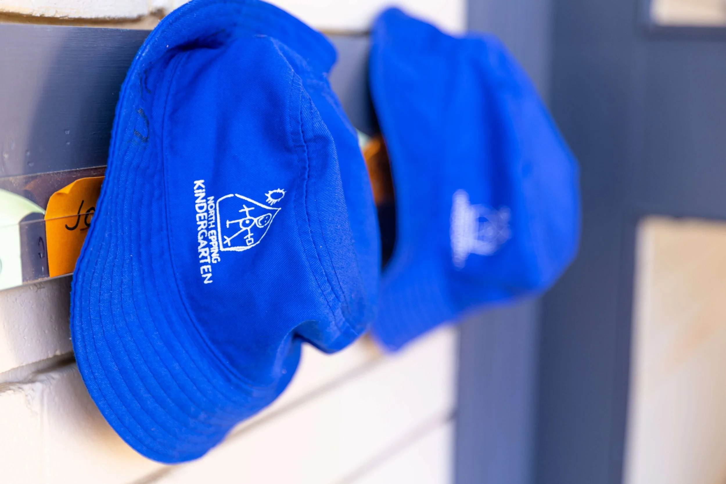 Blue hats with the North Eugene KinderCare logo hanging on a wall.