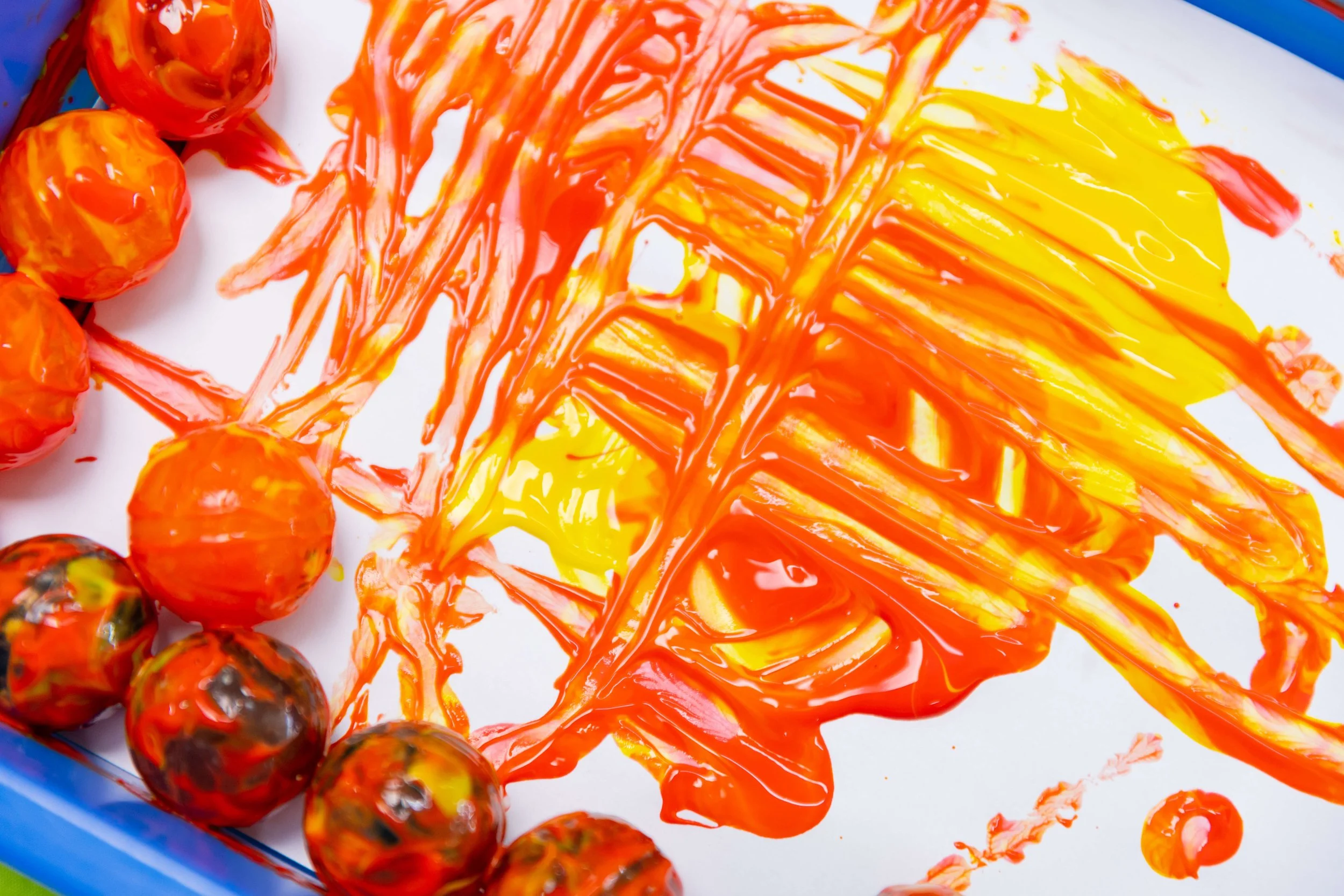 Painted orange and yellow abstract design on paper with a border of multicolored marbles.