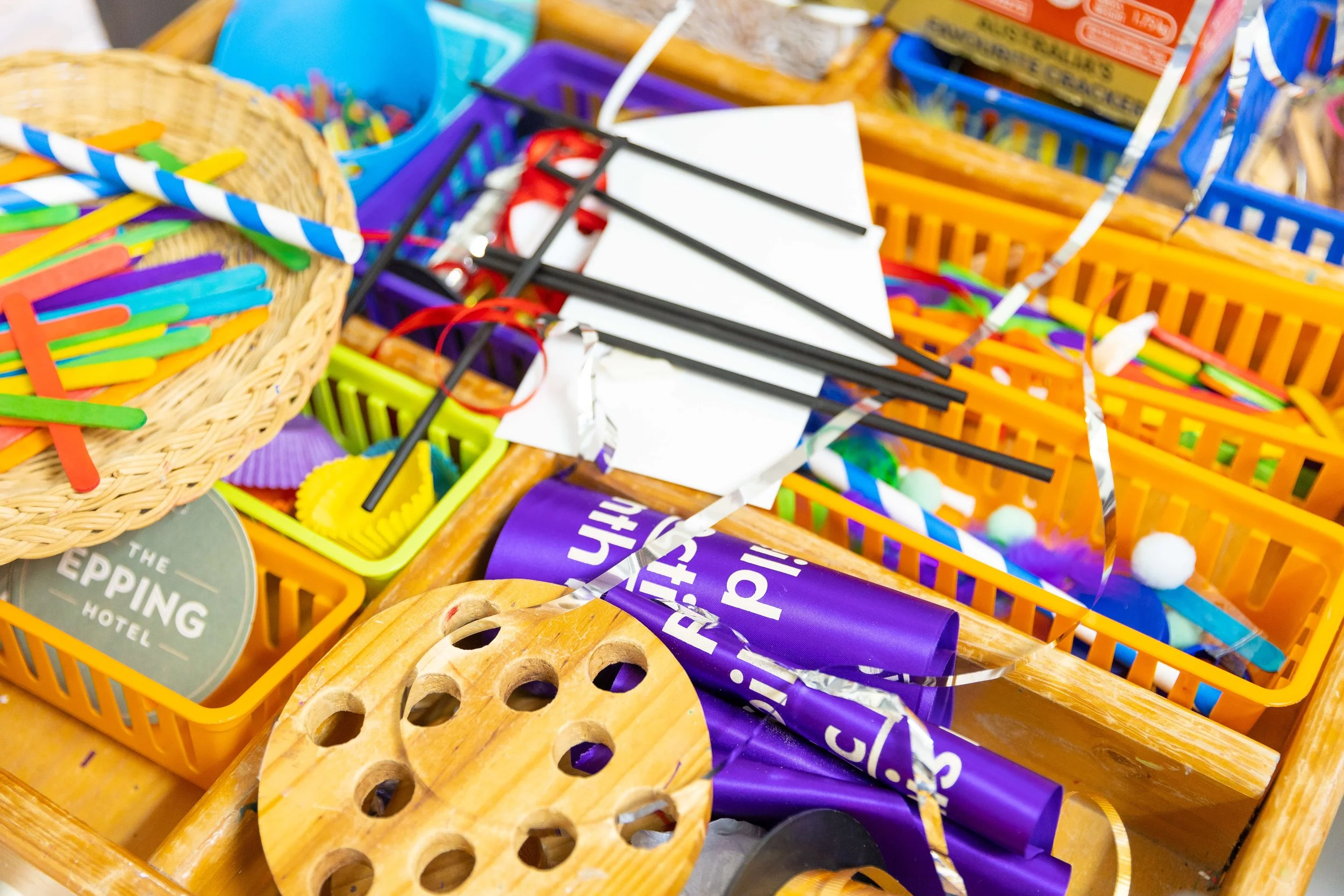Colorful party supplies including paper straws, confetti, and various small decorative items in baskets and containers.