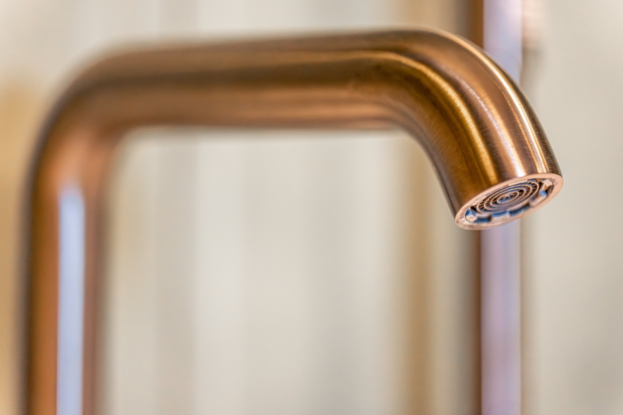 Close-up of a metallic copper faucet spout with a circular aerator at the end.