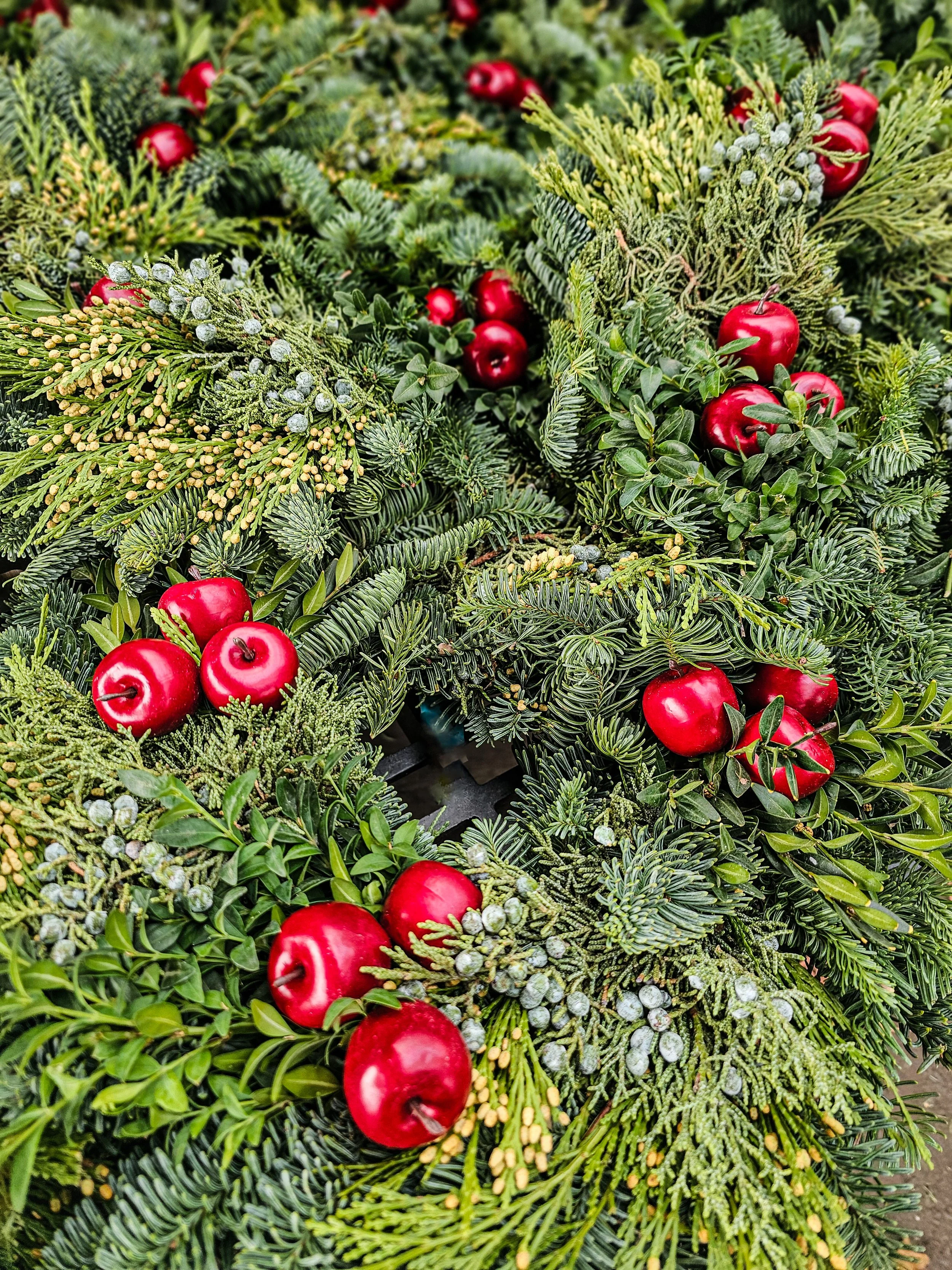 Close-up of a Christmas wreath made of evergreen branches adorned with red apples and small silver ornaments