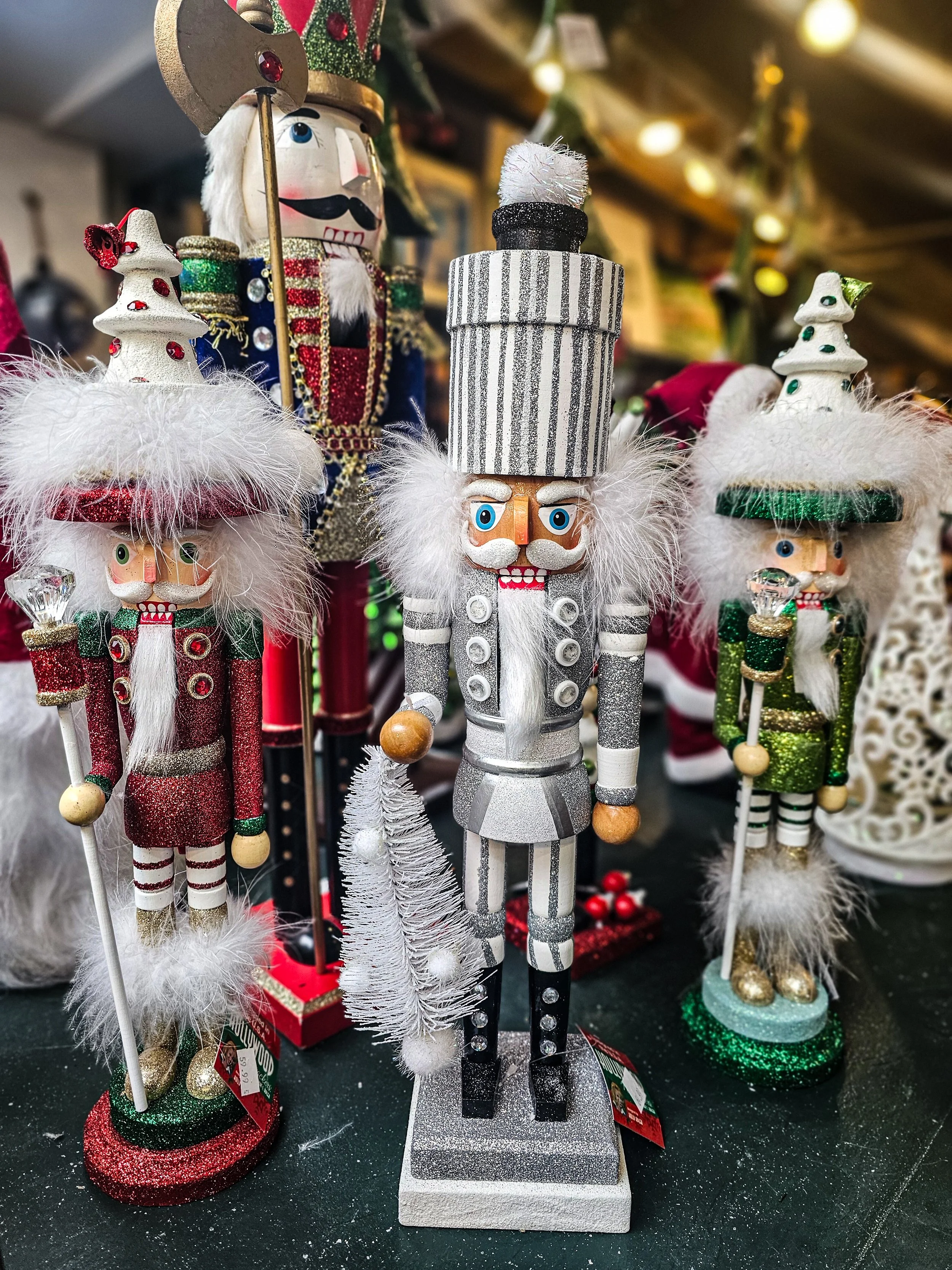 Various Christmas nutcracker decorations, including one with a tall striped hat, a white beard, and a silver and black outfit, with others dressed in red and green, all with white fluffy accents and festive accessories.