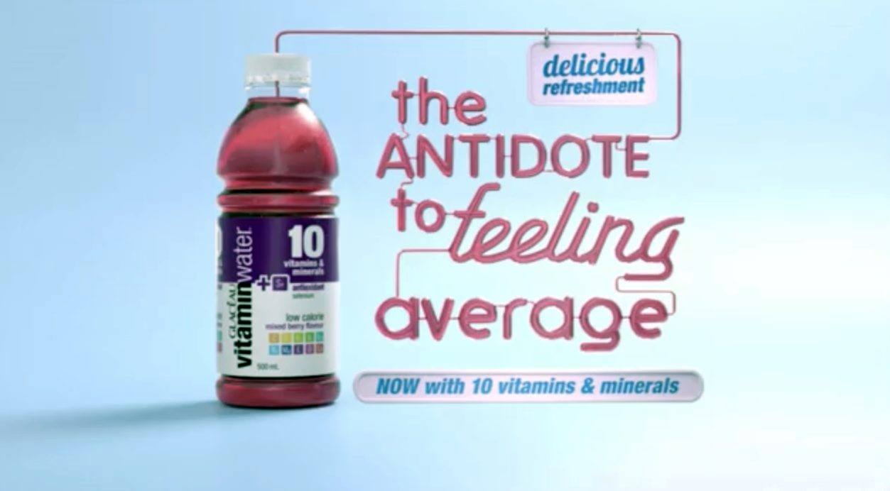 A bottle of vitamin water with a label indicating it contains 10 vitamins and minerals, set against a light blue background. Next to the bottle, there is colorful text that reads 'the ANTIDOTE to feeling average' and a smaller caption that says 'NOW with 10 vitamins & minerals.' A sign at the top right corner says 'delicious refreshment.'