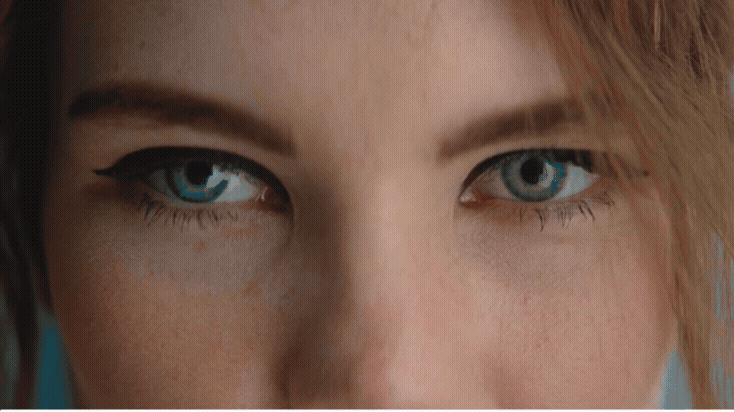 Close-up of a woman's eyes with blue irises, black eyeliner, and freckles on her skin.