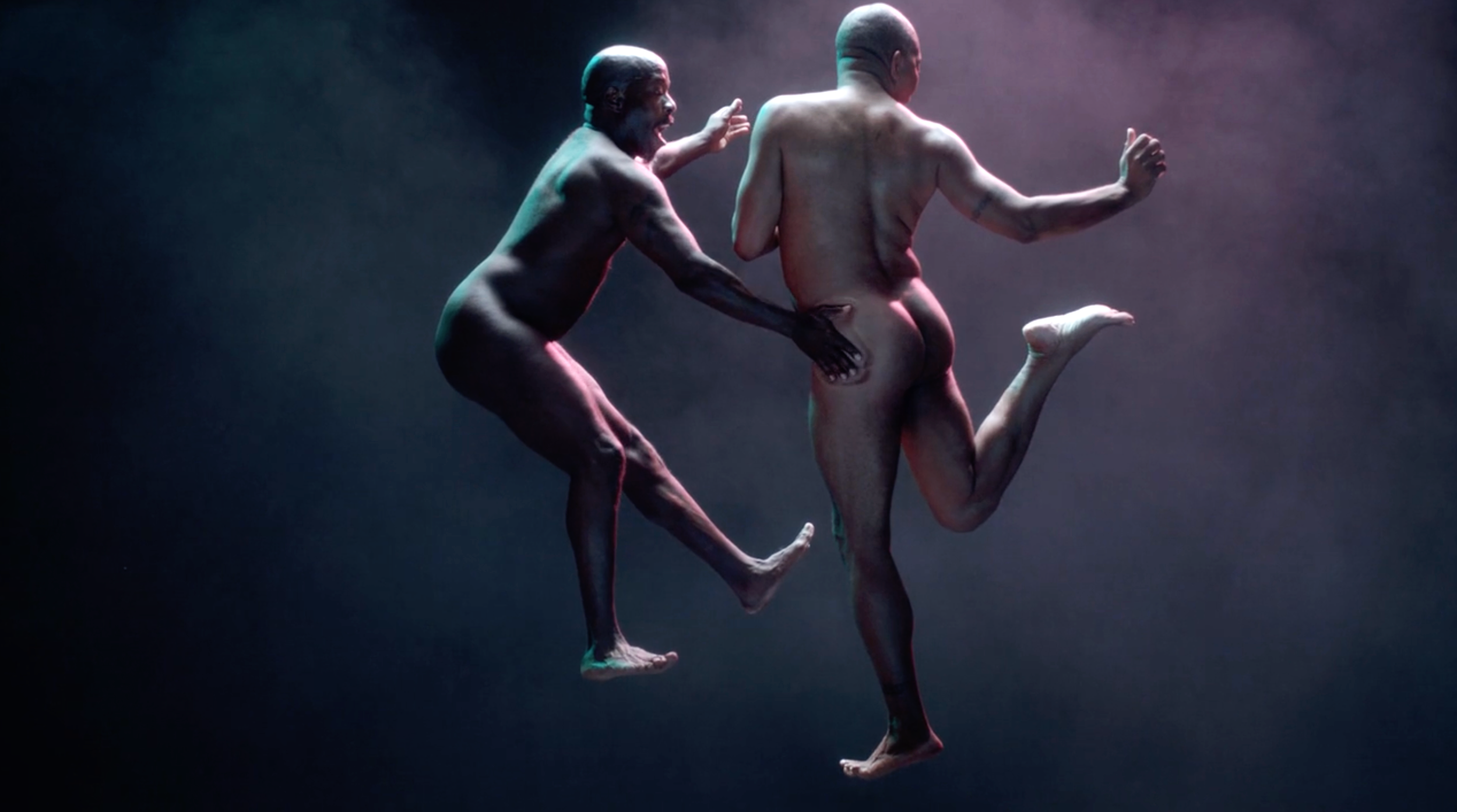Two naked individuals, one with dark skin and the other with lighter skin, appear to be floating or jumping in mid-air against a dark background with soft lighting. They are in expressive poses, with one reaching out and the other with their back turned.