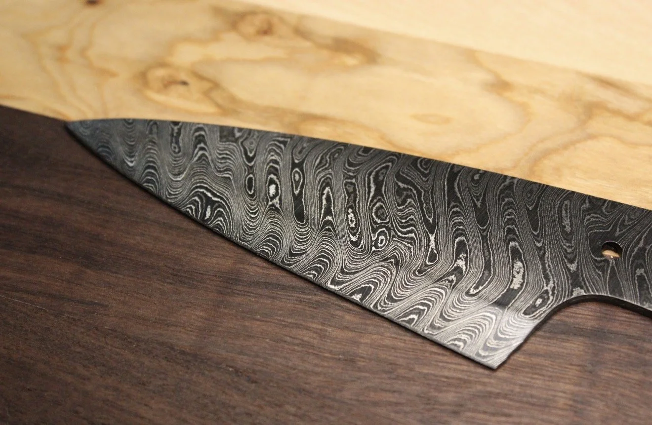 Close-up of a patterned Damascus steel knife resting on a wooden cutting board