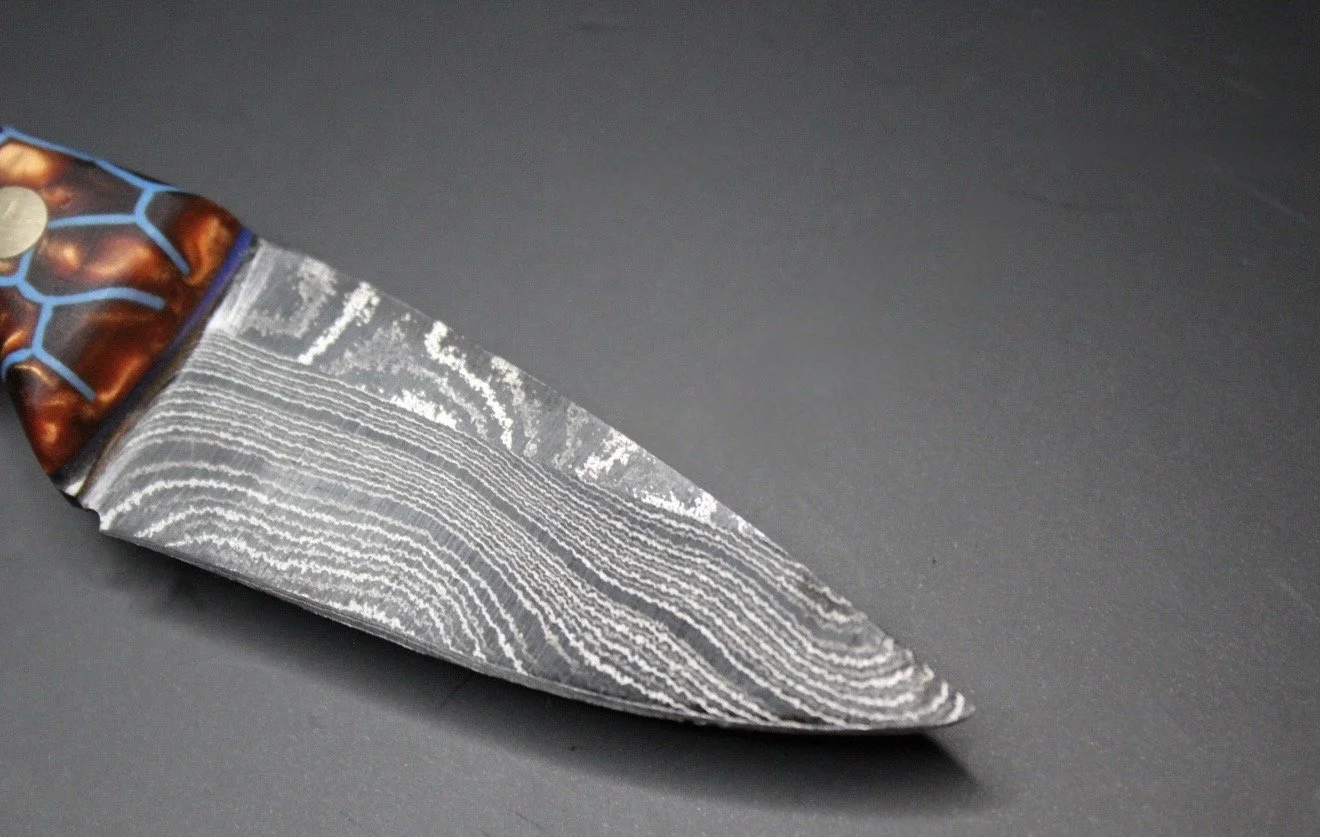 Close-up of a Damascus steel knife with a patterned blade and a decorative handle.