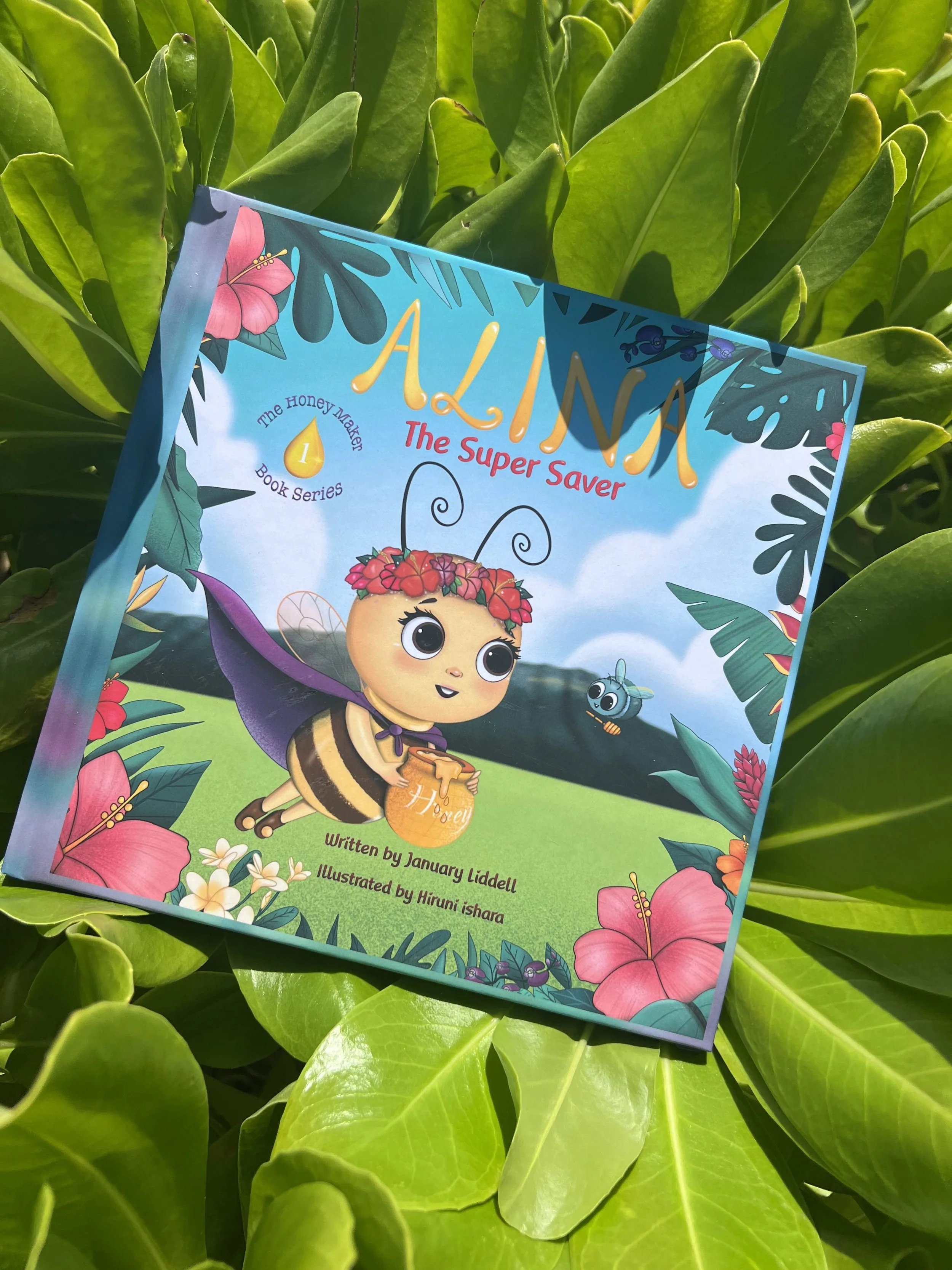 Colorful children's book titled 'Alina The Super Saver' with an illustration of a bee character wearing a purple cape, surrounded by flowers and greenery.