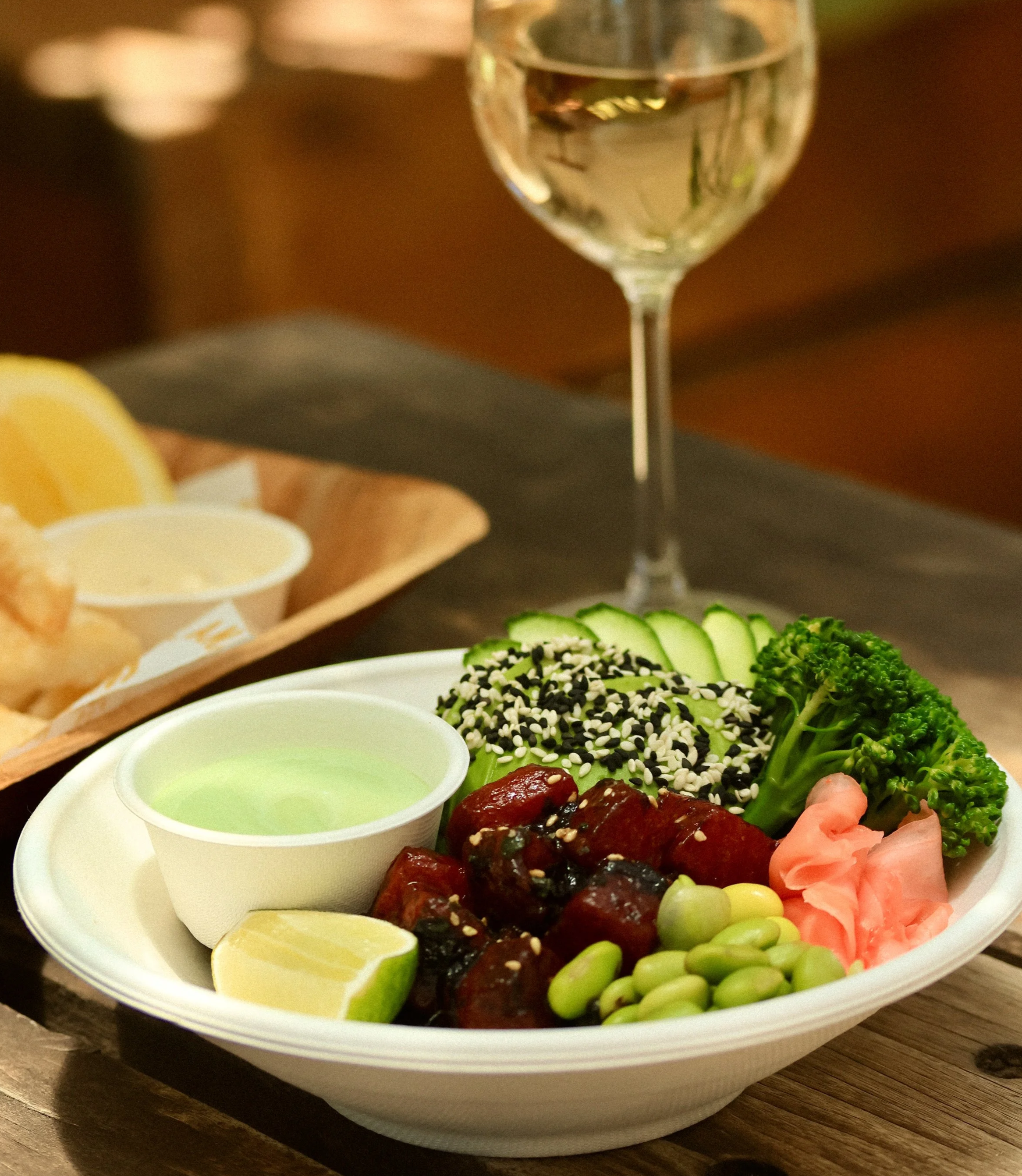 a bowl of marinated watermelon, with fresh greens, pickled ginger, edamame and a glass of wine