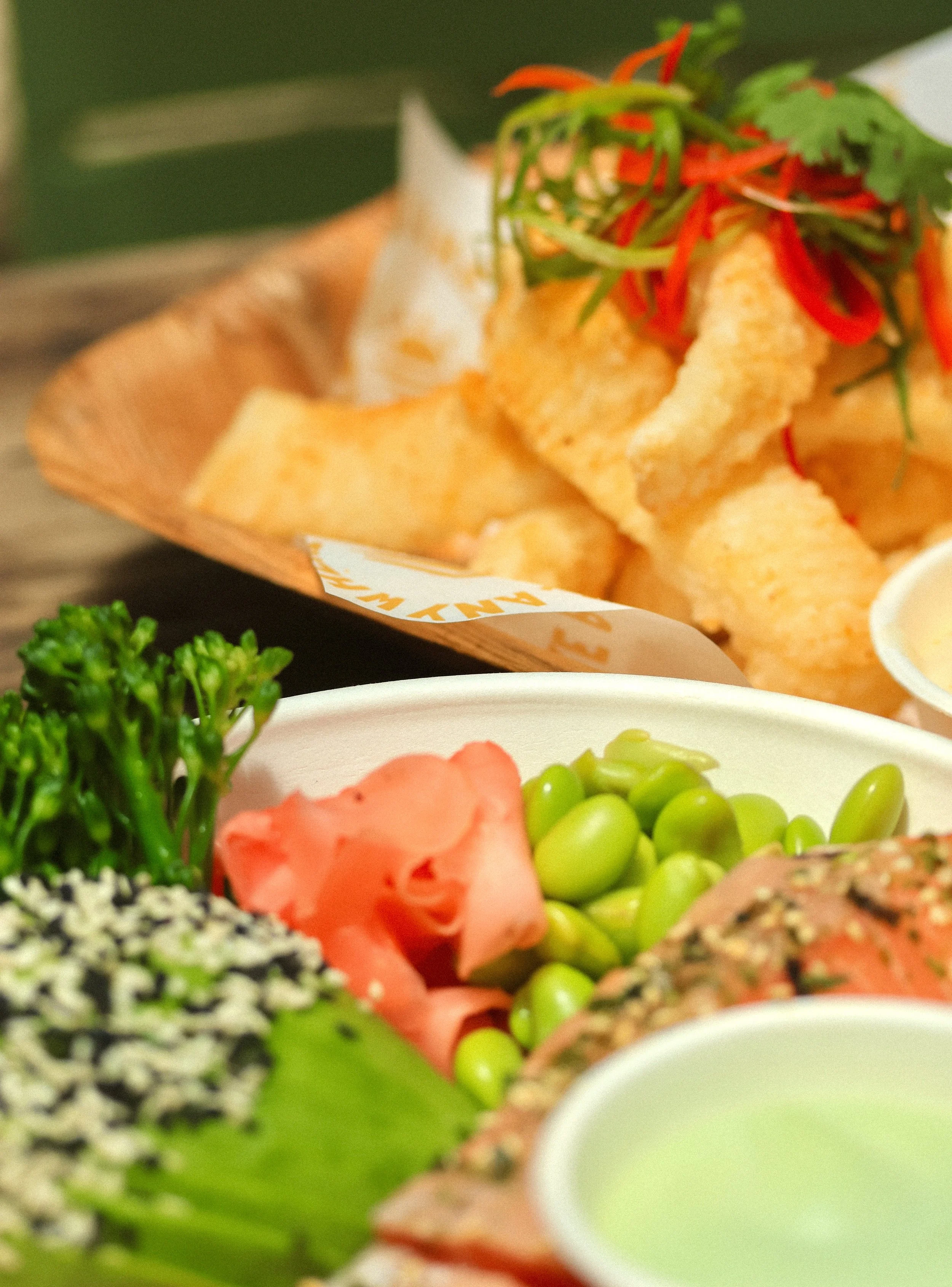 Close-up of a platter with vegetables and sashimi, and a basket of fried fish fillets garnished with red chili and herbs in the background.