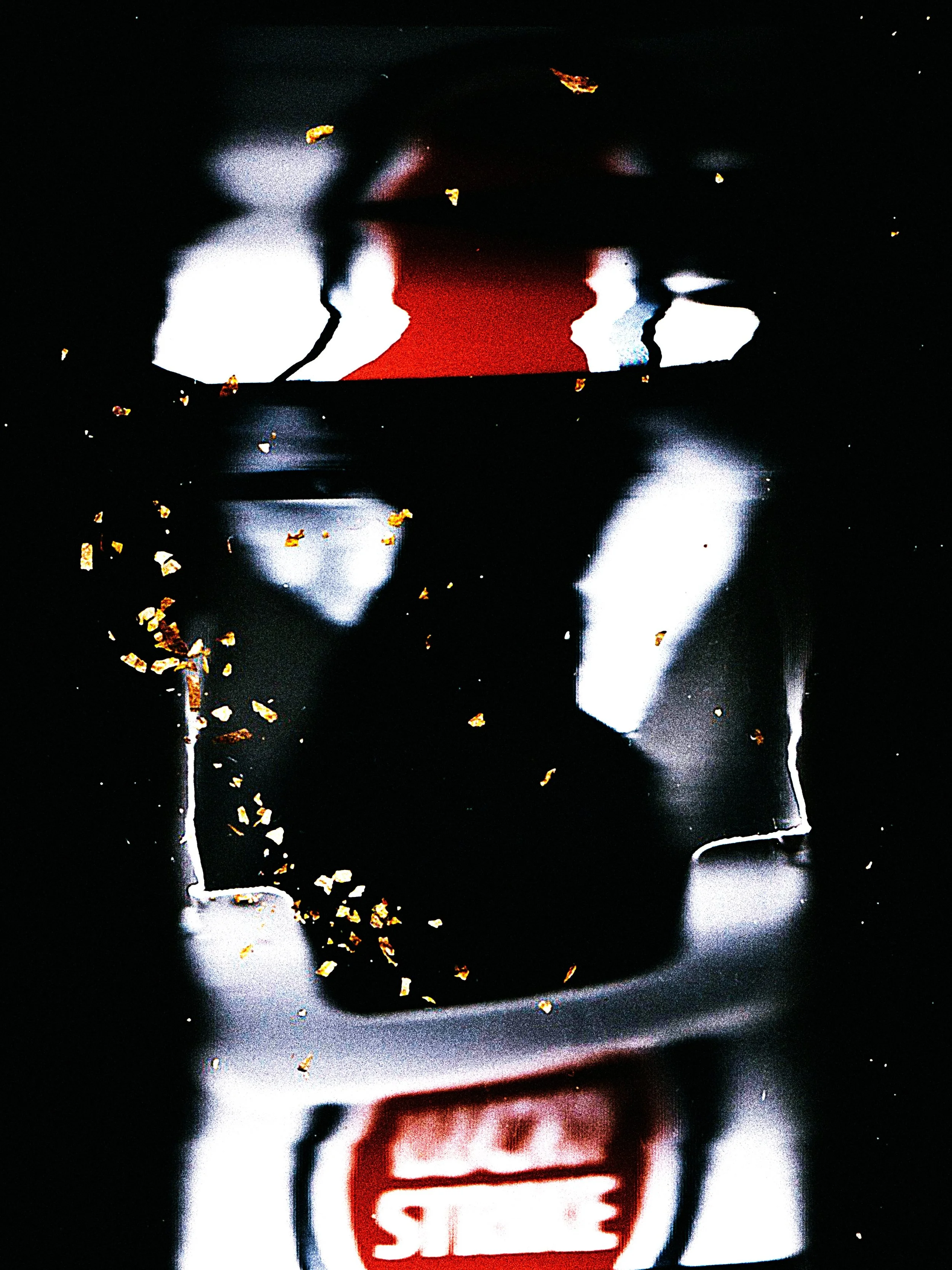 Close-up of a reflective black surface with scattered gold flakes, showing distorted reflections of white and red objects.
