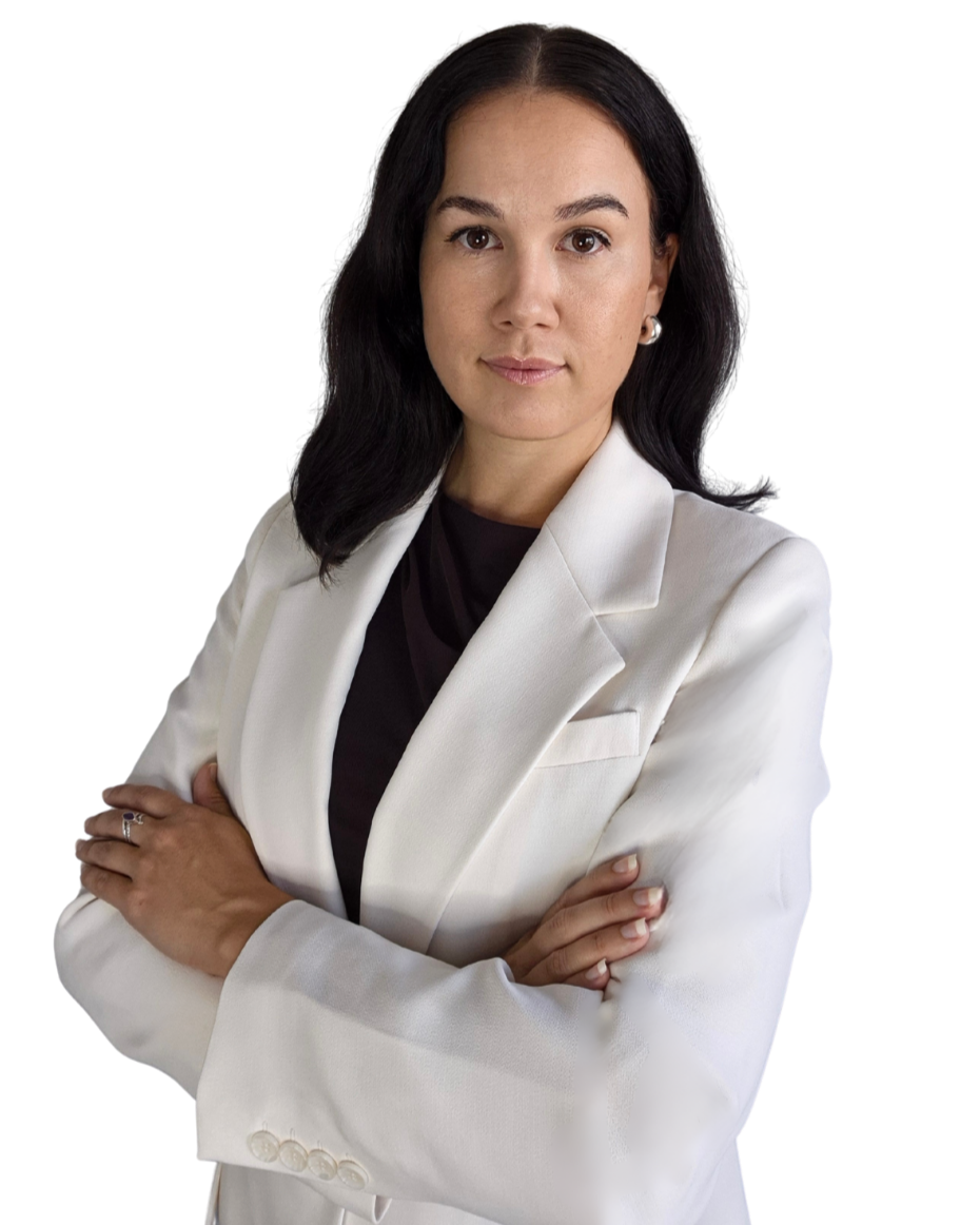 A confident woman with black hair styled in loose waves wearing a white blazer and black top, standing with her arms crossed against a black and red background.